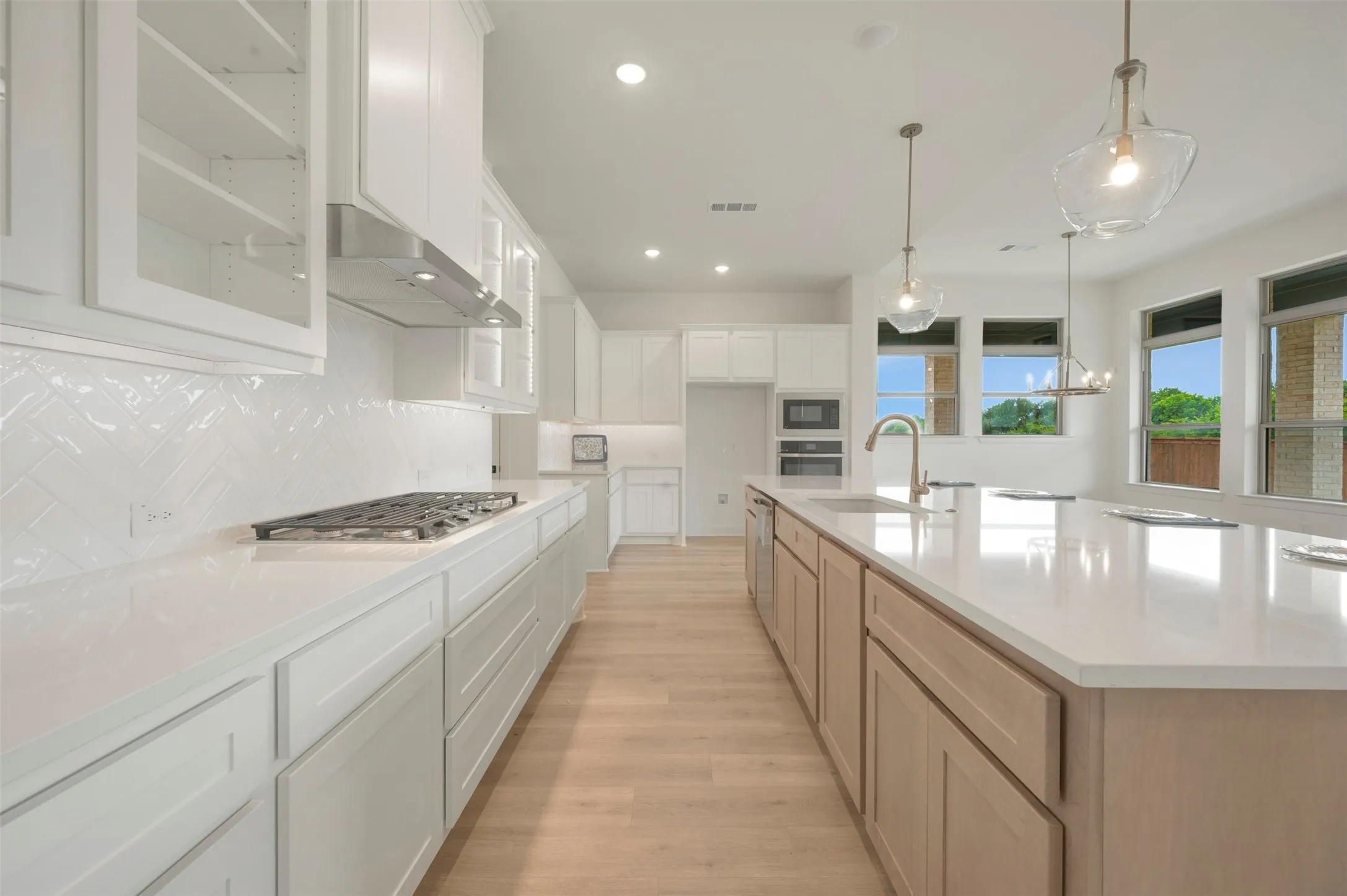 Modern kitchen featuring an extended island with light wood-finish cabinetry, quartz countertops, and stainless steel appliances