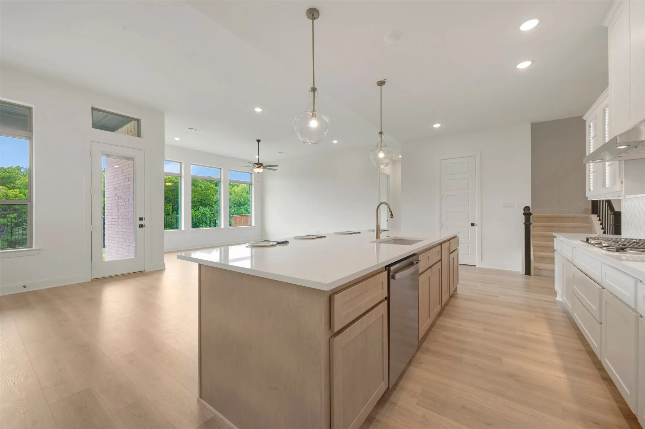 Kitchen island featuring a stainless steel sink with a high-arc faucet, integrated dishwasher, and light wood cabinetry