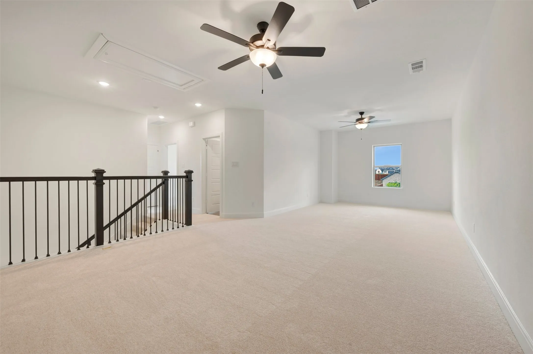 Spacious carpeted bonus room with a wrought iron railing, two ceiling fans with integrated lighting, and recessed ceiling lights