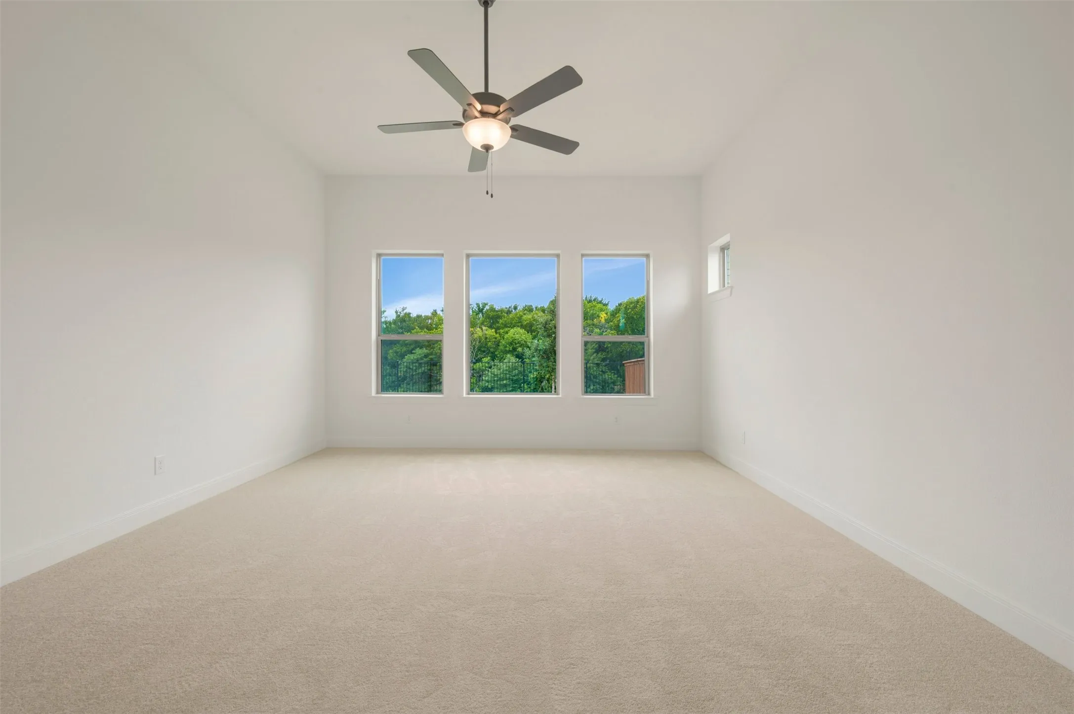 Spacious room featuring neutral carpeting, a ceiling fan with integrated lighting, and three tall windows providing natural illumination