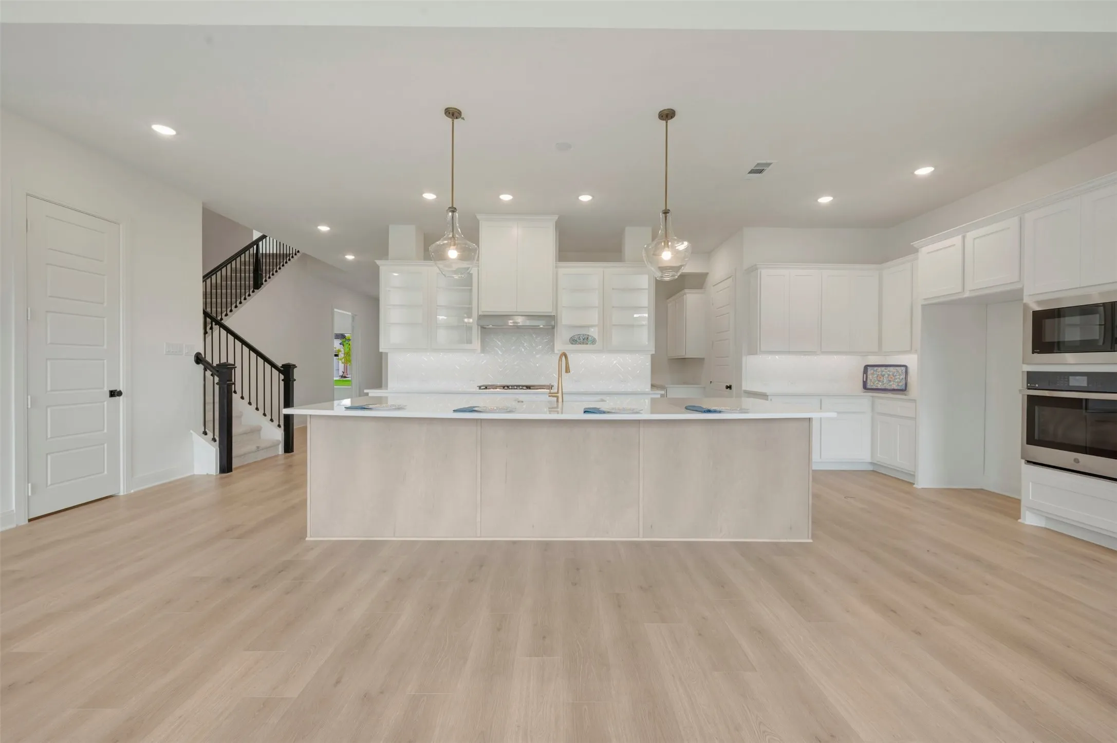 Spacious kitchen featuring an expansive center island, white cabinetry, built-in stainless steel appliances, and two pendant light fixtures