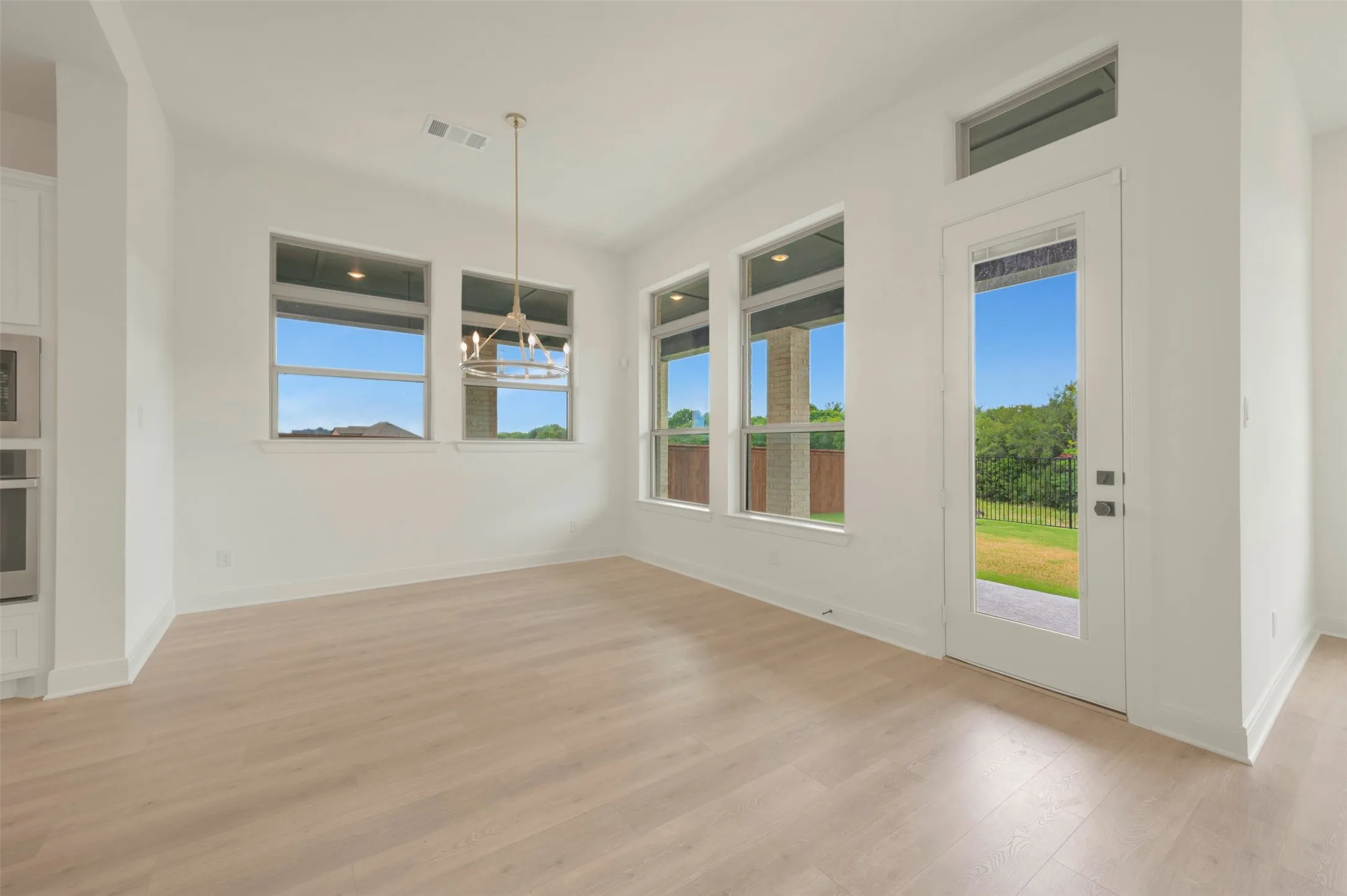 Open-concept interior featuring light wood-finish flooring, multiple large windows, and a glass-paneled exterior door
