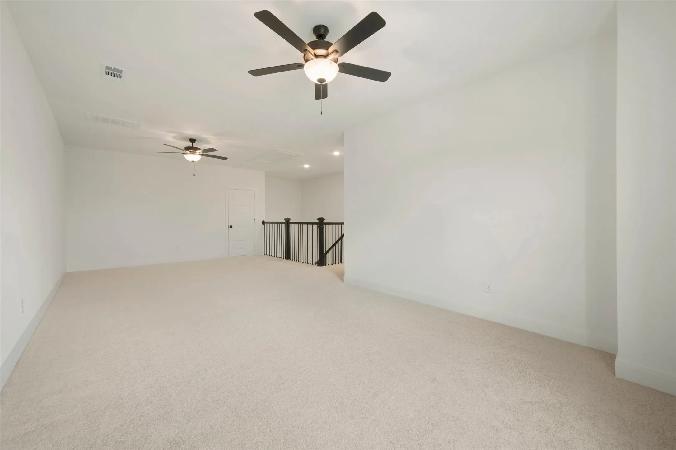 Expansive upstairs area featuring light carpeting, two ceiling fans with integrated lighting, and a contemporary black metal baluster railing