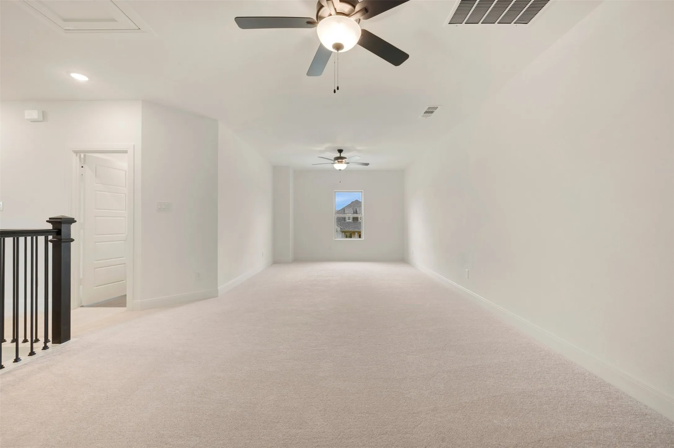 Spacious carpeted room featuring multiple ceiling fans with integrated lighting, a single window, white walls, and a black railing