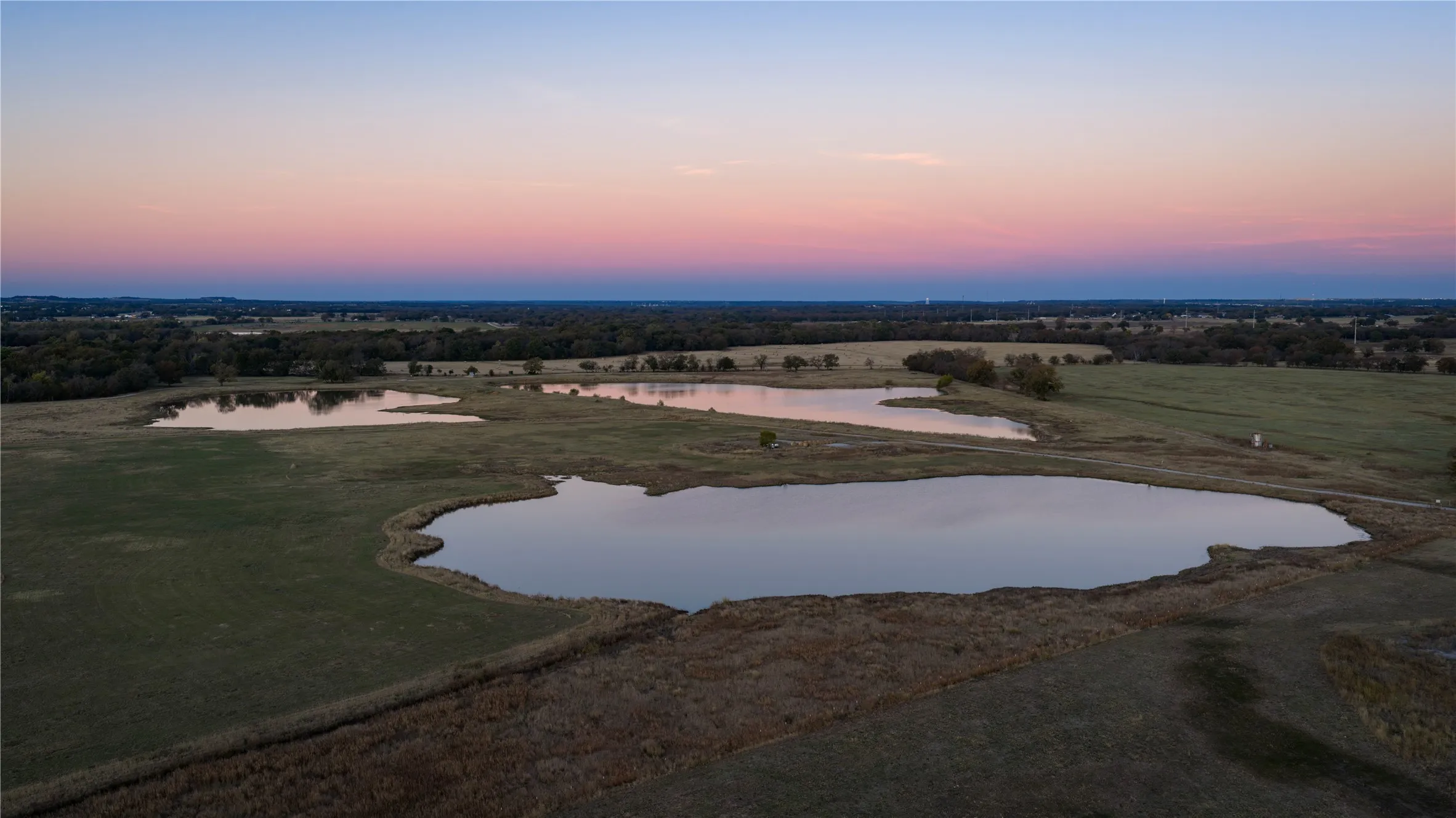 Sunset aerial view highlighting pond and open pasture.