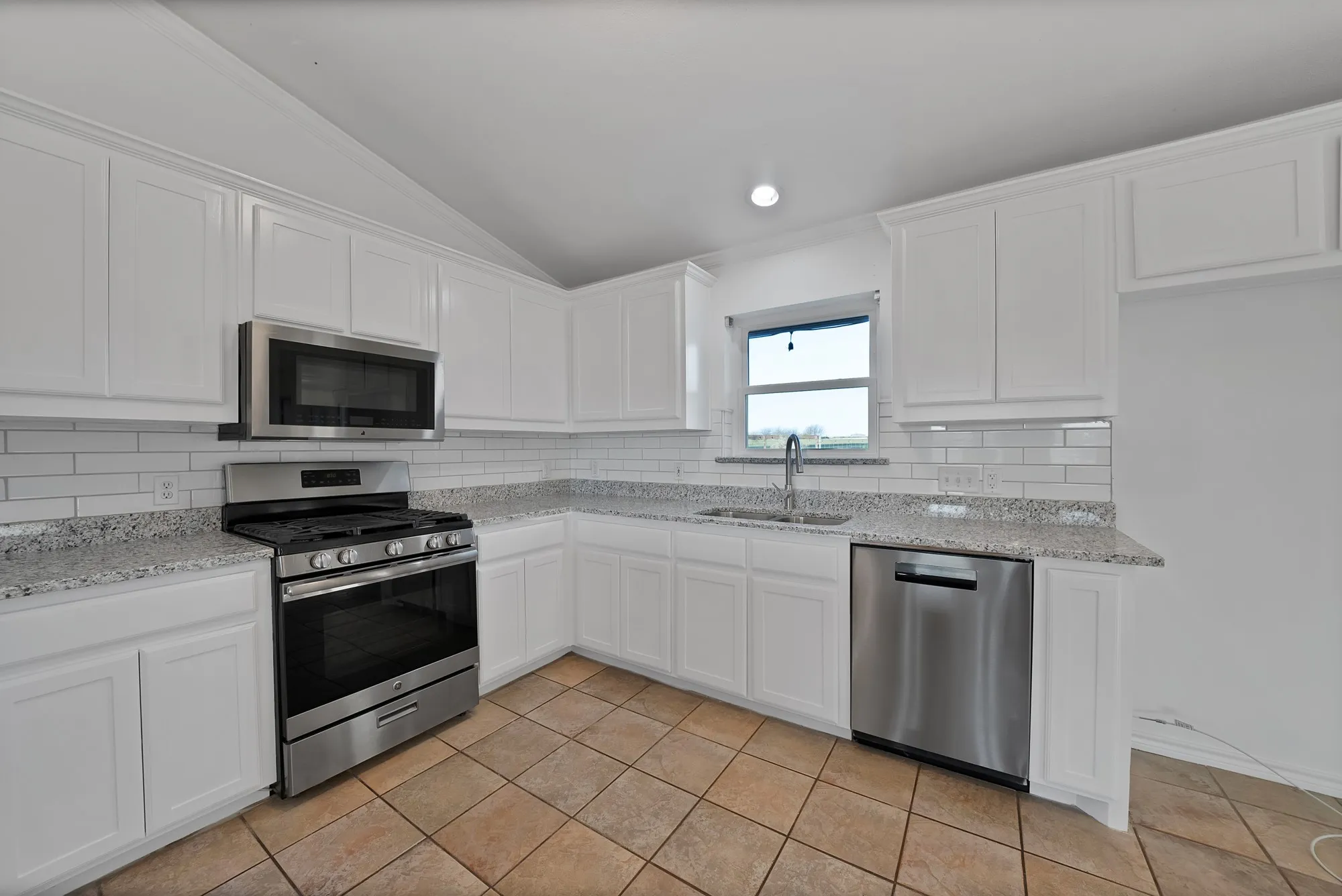 Kitchen featuring stainless steel appliances, lofted ceiling, white cabinets, light stone counters, and backsplash