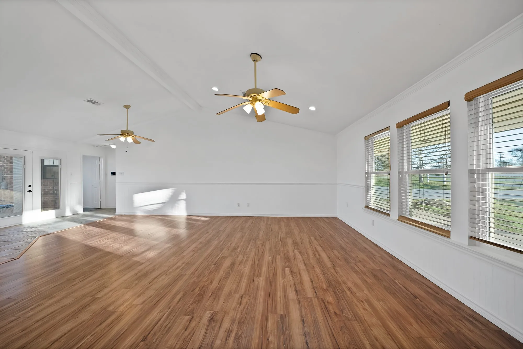 Unfurnished living room featuring dark wood-type flooring, lofted ceiling with beams, and ceiling fan