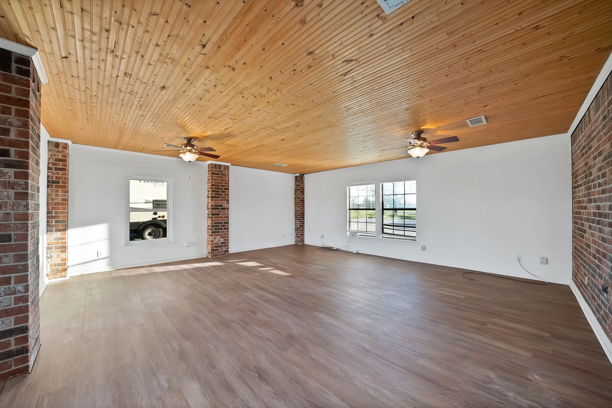 Unfurnished living room featuring brick wall, dark wood-type flooring, a ceiling fan, and wooden ceiling