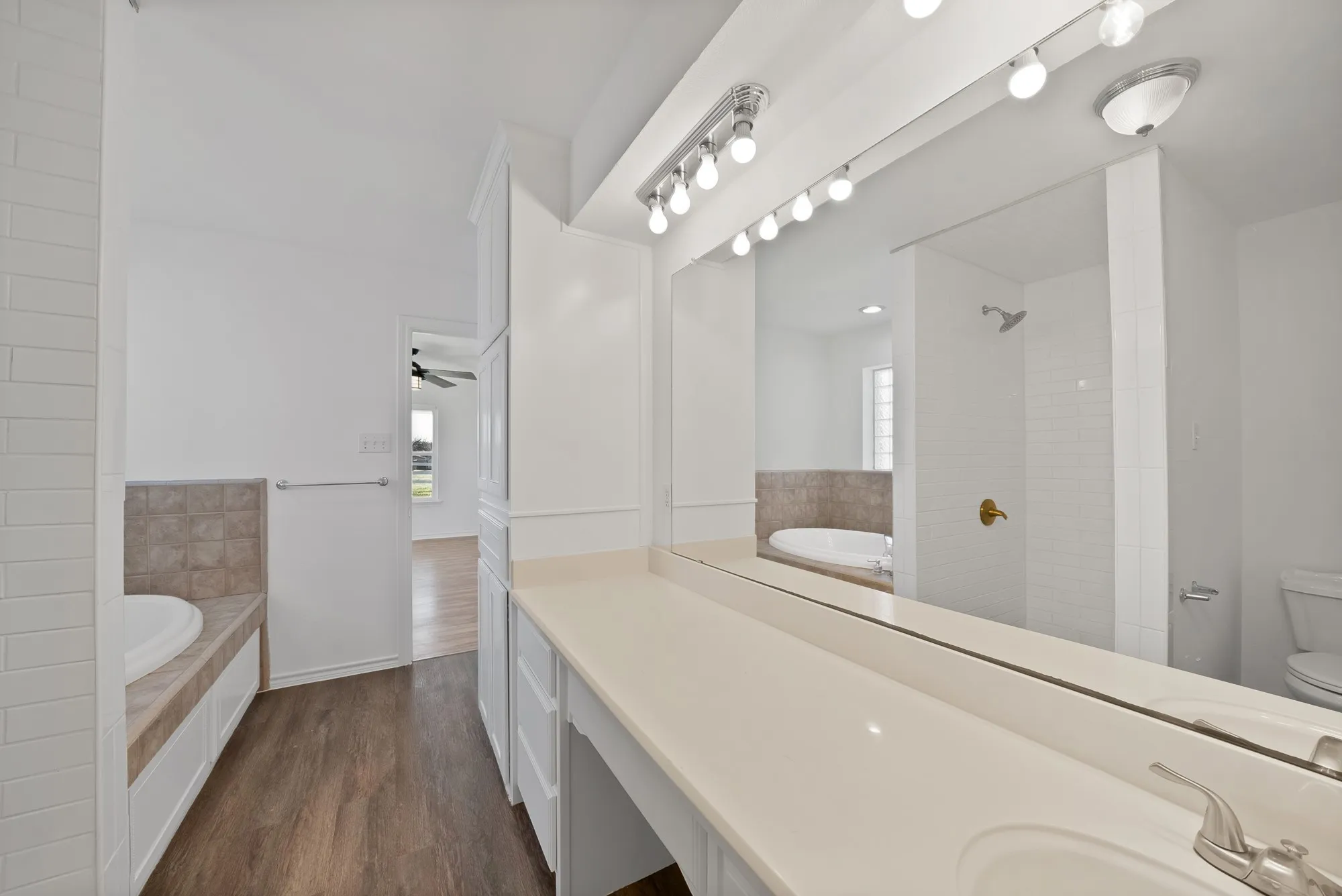 Full bath featuring a garden tub, vanity, dark wood-style floors, and tiled shower