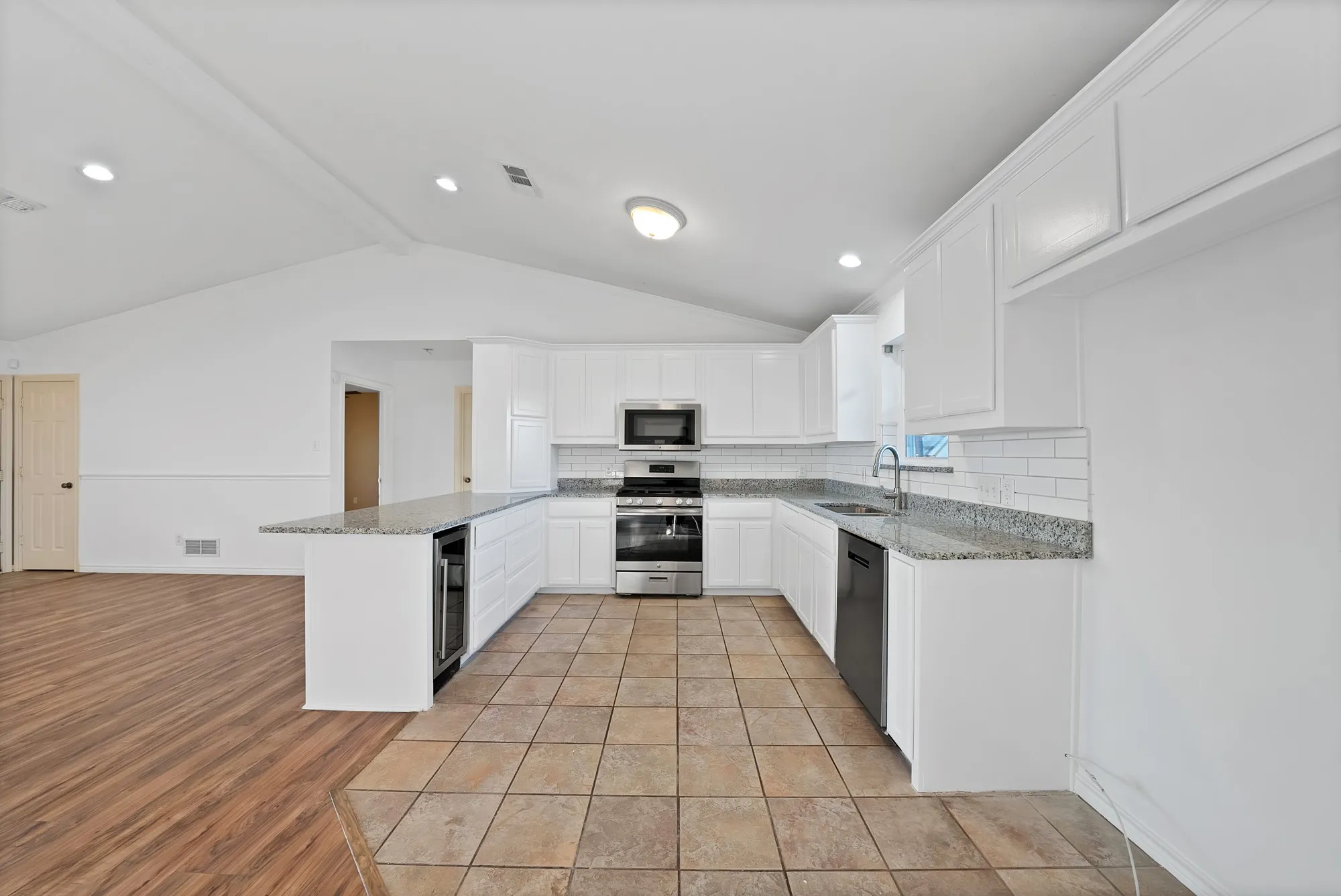 Kitchen with white cabinets, light stone countertops, decorative backsplash, stainless steel appliances, and a peninsula
