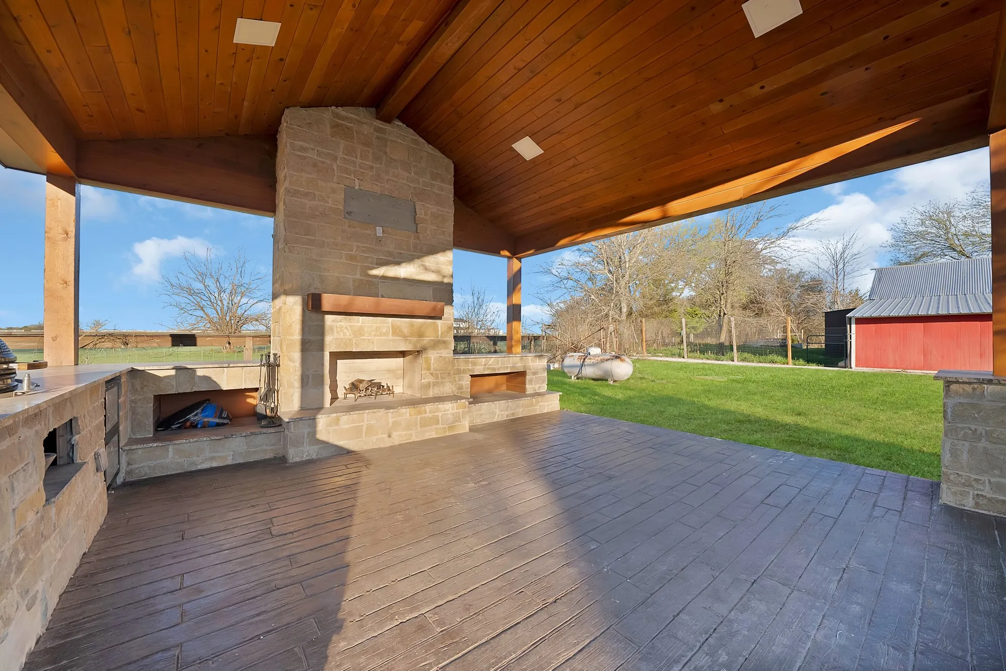 Wooden terrace featuring an outdoor stone fireplace, a yard, and a patio