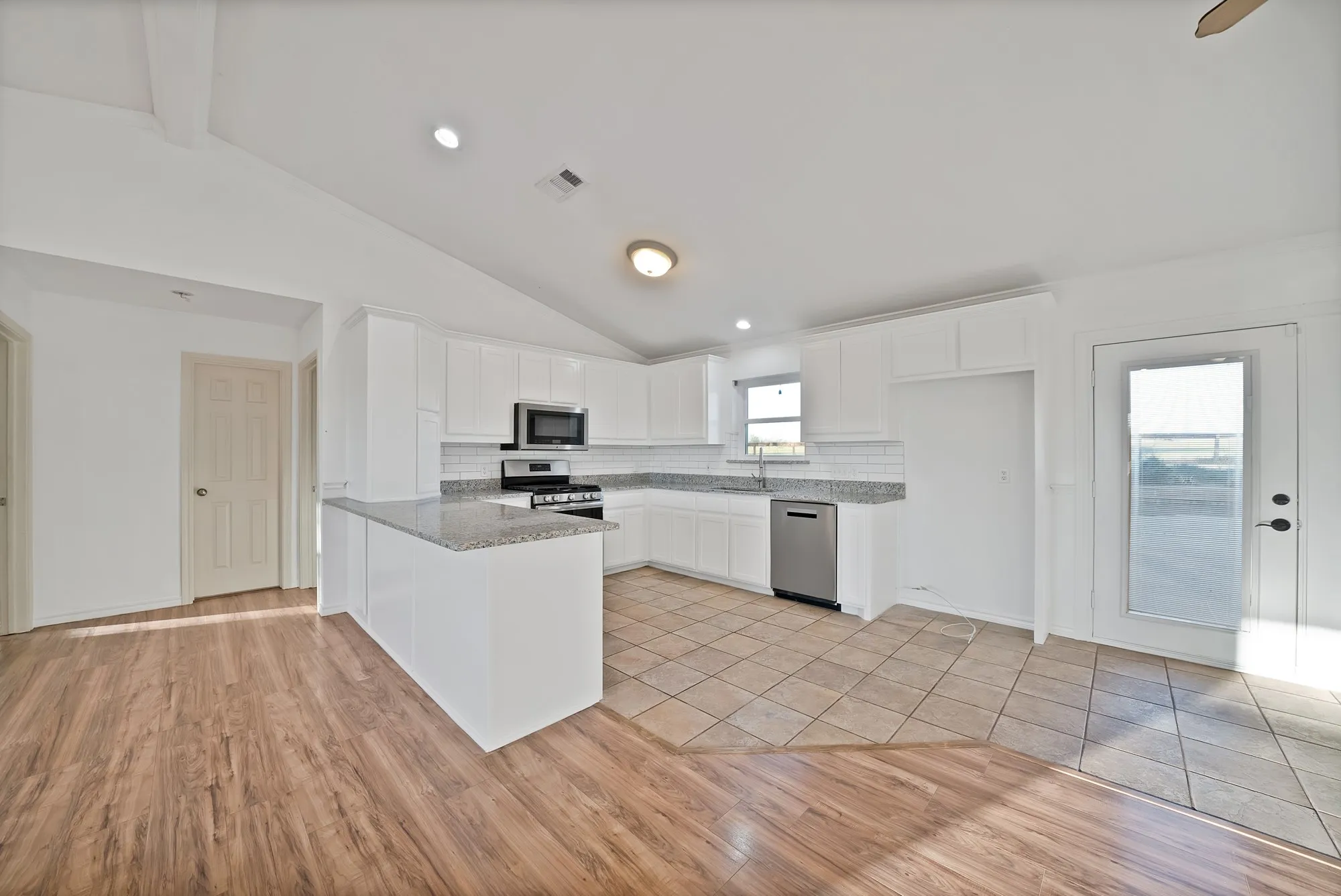 Kitchen with lofted ceiling, white cabinetry, light wood finished floors, decorative backsplash, and stainless steel appliances