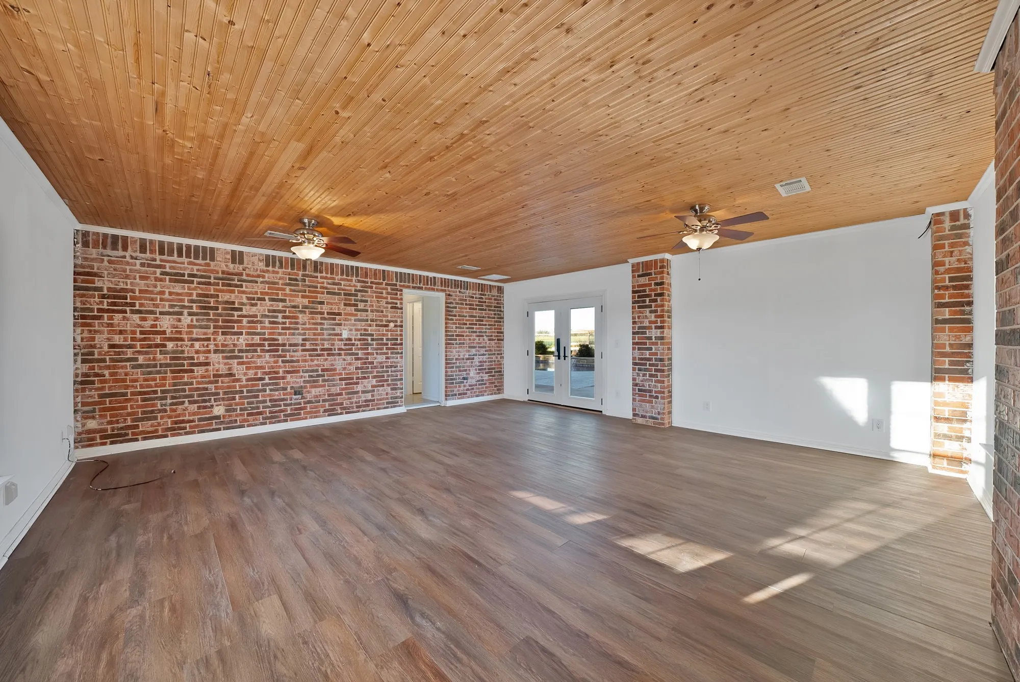 Unfurnished living room featuring brick wall, french doors, wood finished floors, and a ceiling fan