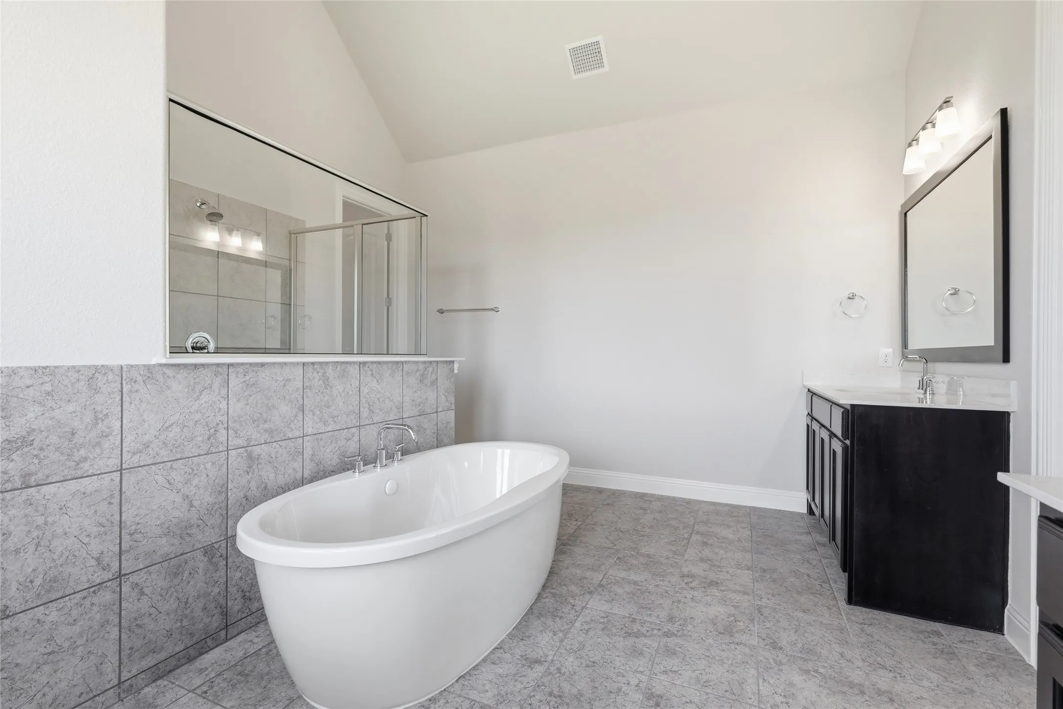 Full bathroom with lofted ceiling, vanity, a stall shower, a freestanding bath, and tile walls