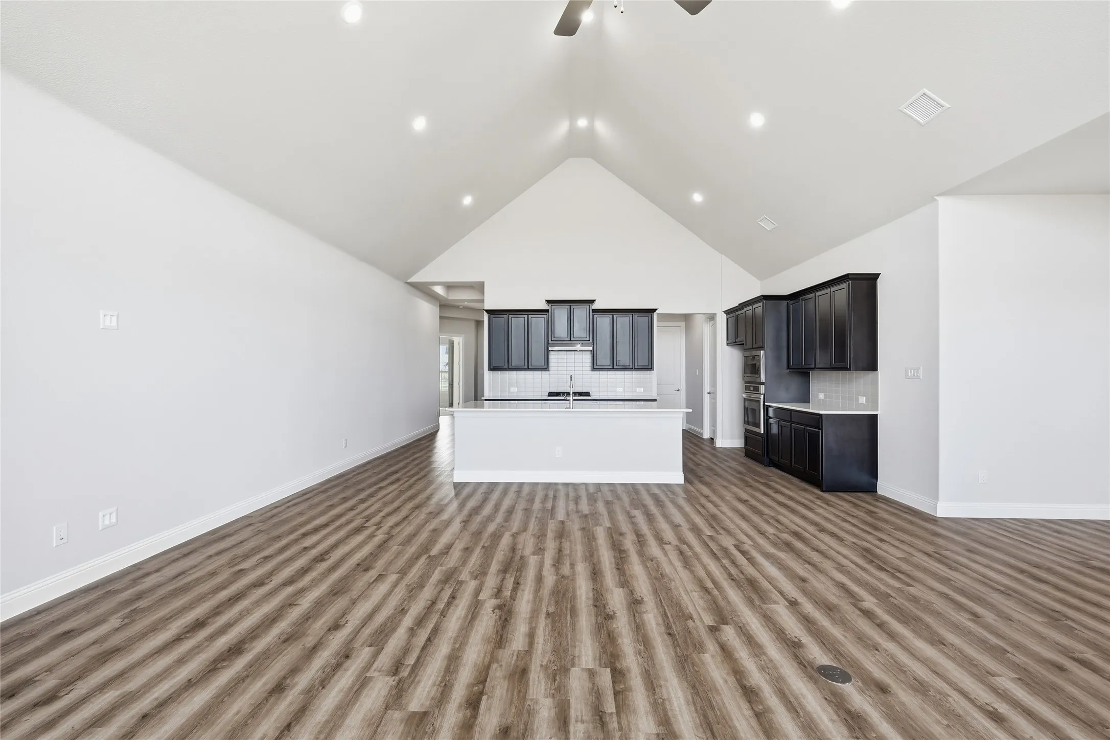 Unfurnished living room featuring a ceiling fan, a high ceiling, and dark wood-style floors