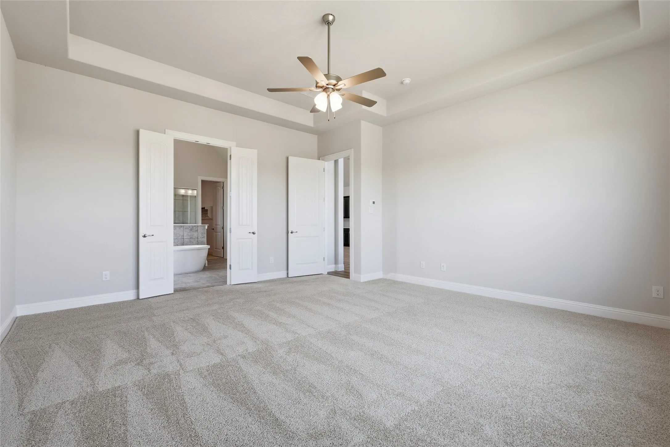 Unfurnished bedroom featuring a tray ceiling, light carpet, a ceiling fan, and connected bathroom