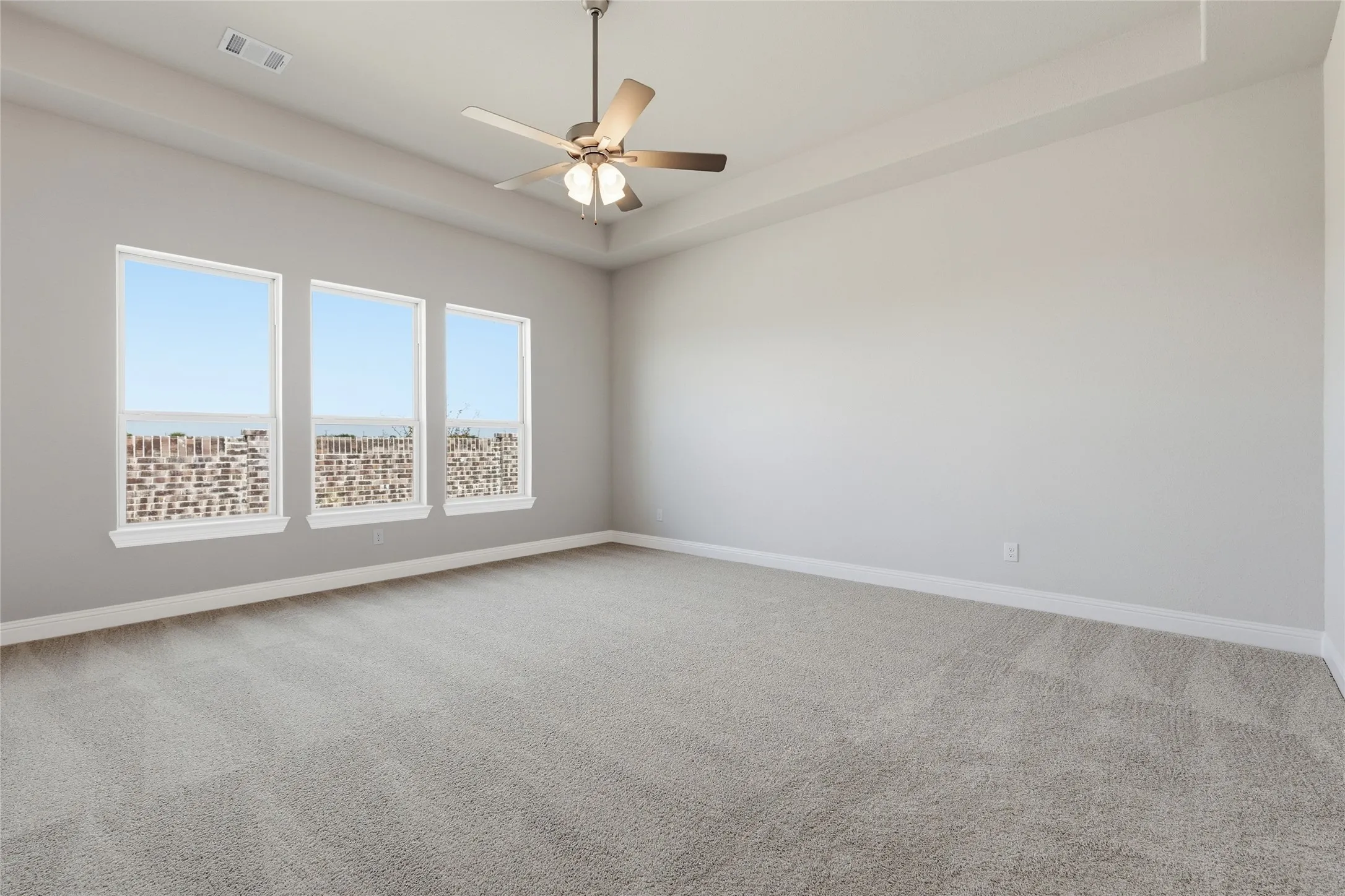 Unfurnished room featuring a raised ceiling, light colored carpet, and a ceiling fan