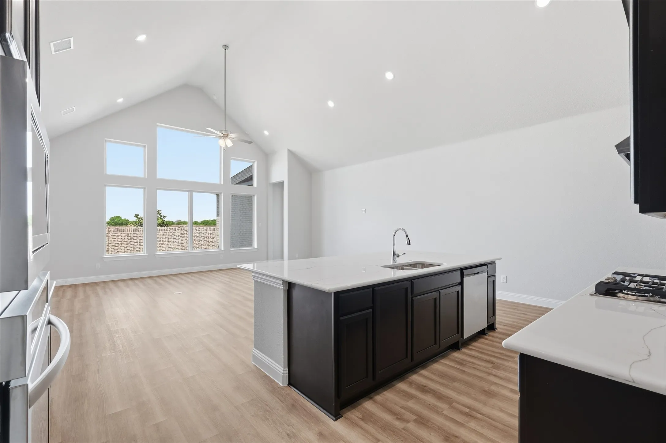 Kitchen with a high ceiling, dark cabinets, open floor plan, a center island with sink, and light wood-style flooring