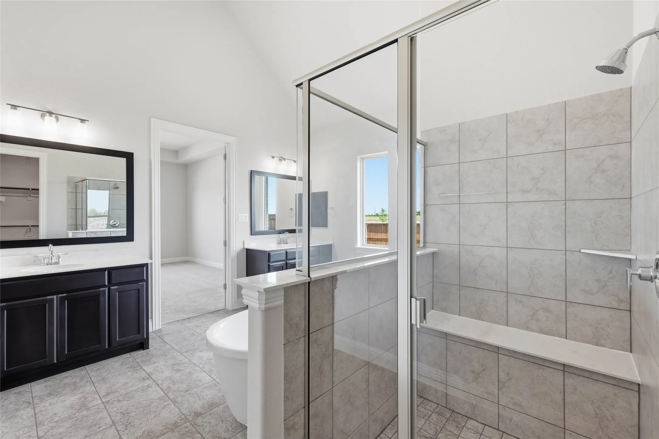 Bathroom featuring a stall shower, a soaking tub, two vanities, and light tile patterned floors
