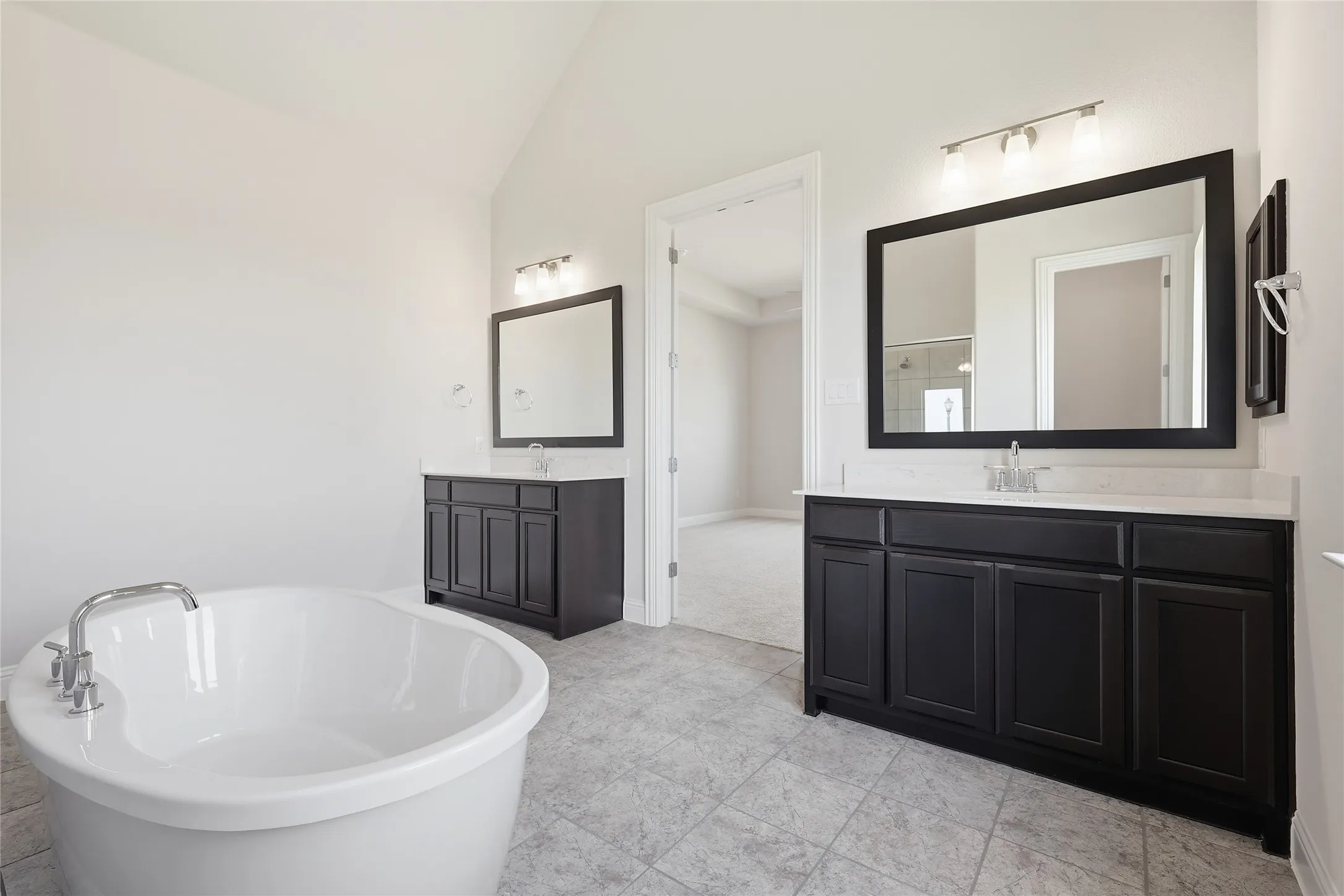Bathroom featuring two vanities, vaulted ceiling, and a freestanding tub