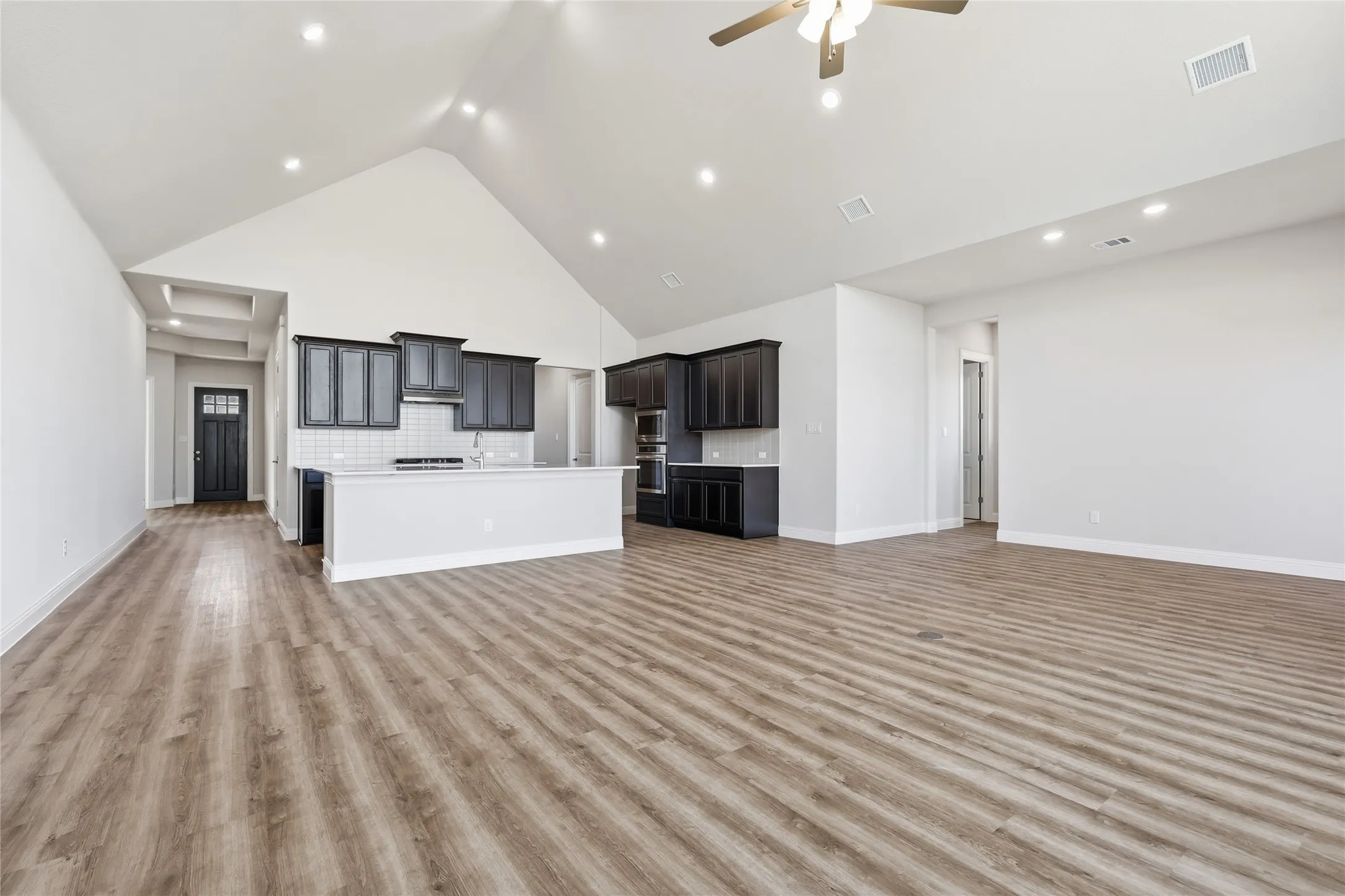 Unfurnished living room with a high ceiling, a ceiling fan, light wood finished floors, and recessed lighting