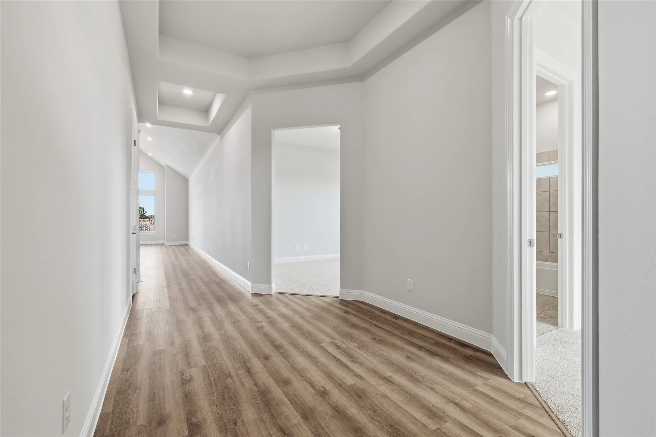 Corridor featuring recessed lighting, light wood finished floors, and a raised ceiling