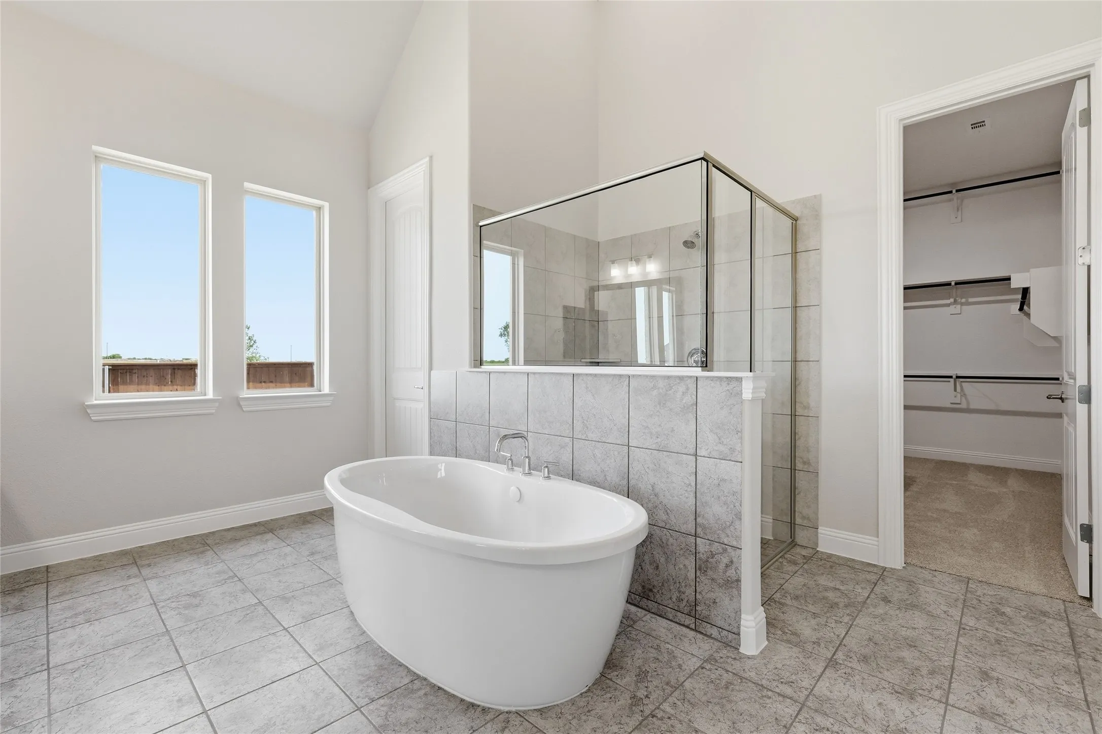Bathroom with a stall shower, a walk in closet, a freestanding bath, tile walls, and light tile patterned floors