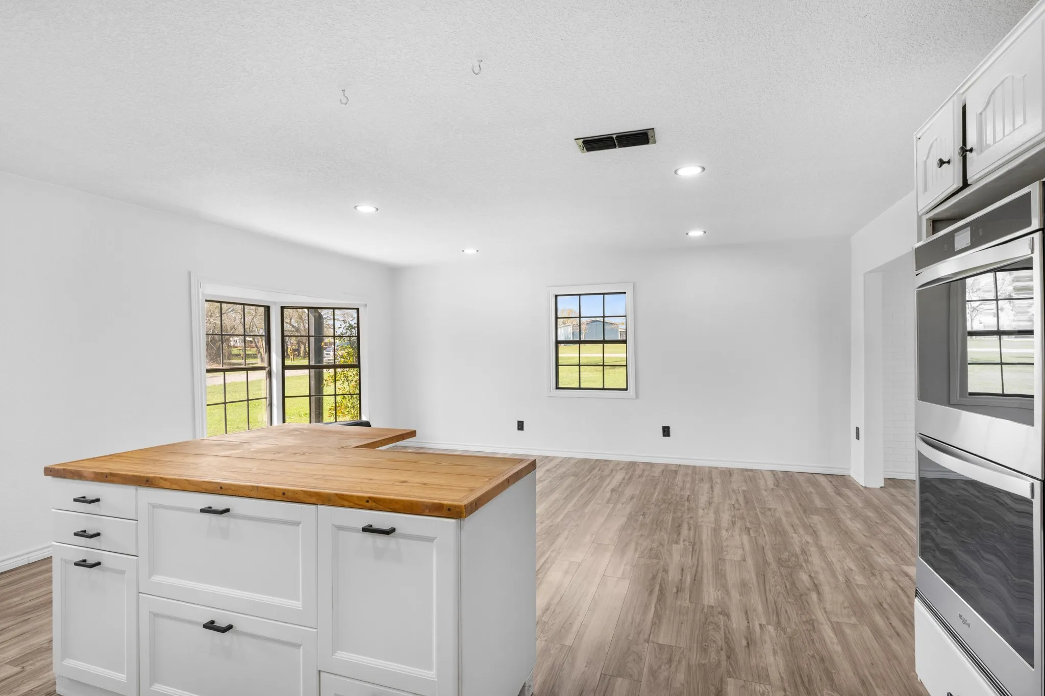 Kitchen with stainless steel double oven, butcher block counters, white cabinets, open floor plan, and recessed lighting