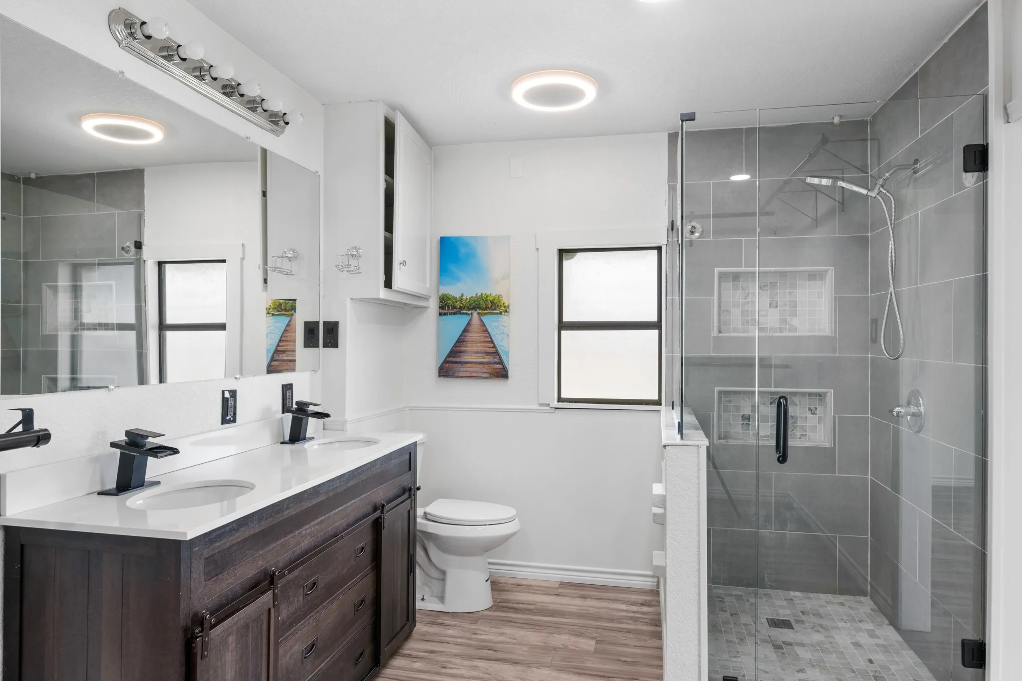 Full bath featuring double vanity, a shower stall, and light wood-type flooring