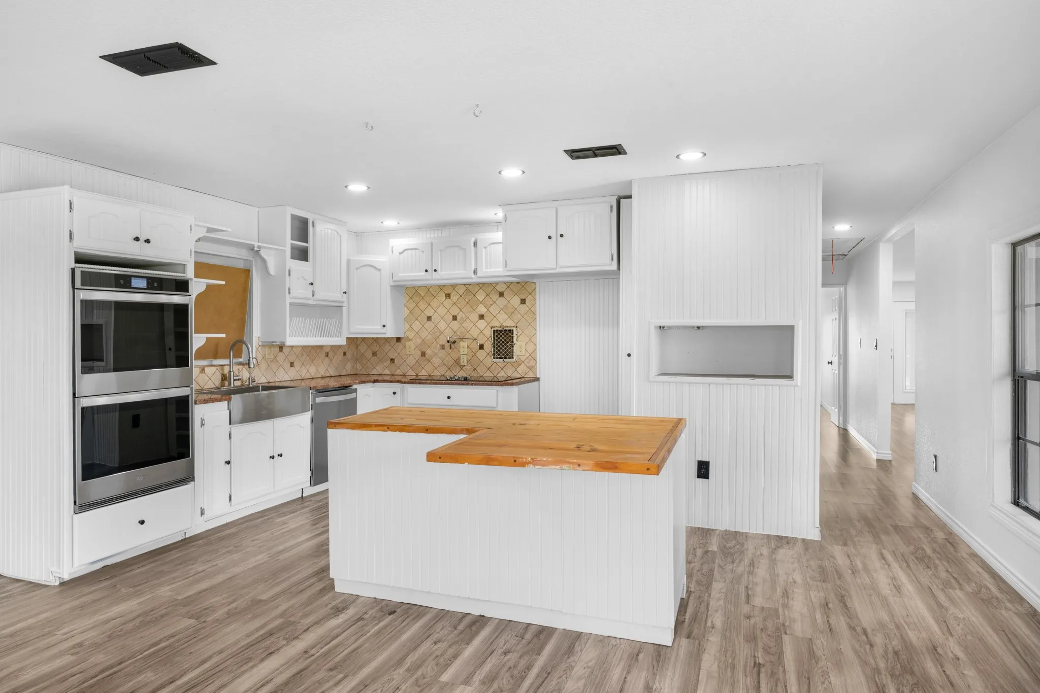 Kitchen with a center island, light wood finished floors, white cabinetry, stainless steel appliances, and backsplash