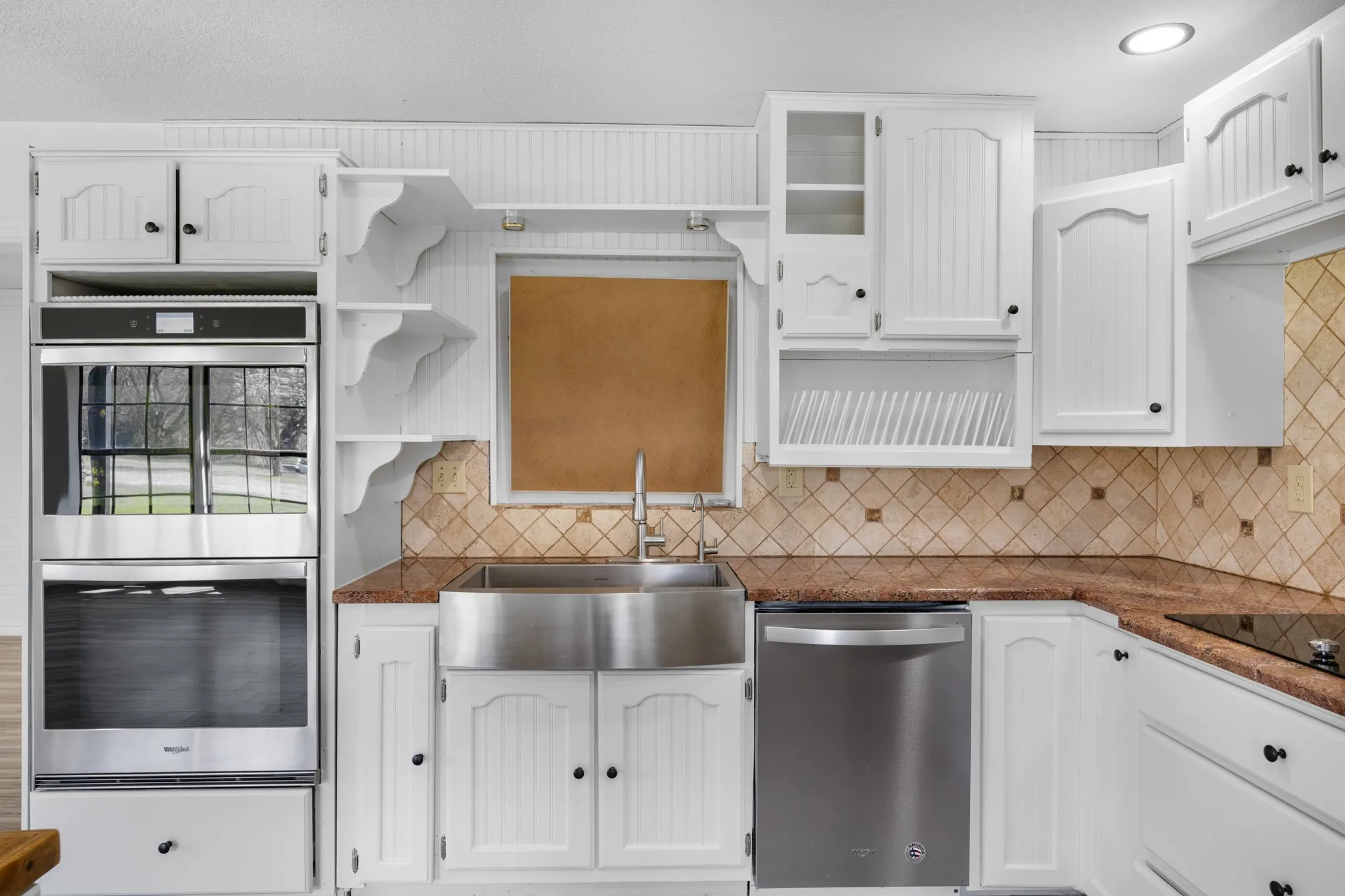 Kitchen with stainless steel appliances, white cabinetry, open shelves, dark stone counters, and glass fronted cabinets