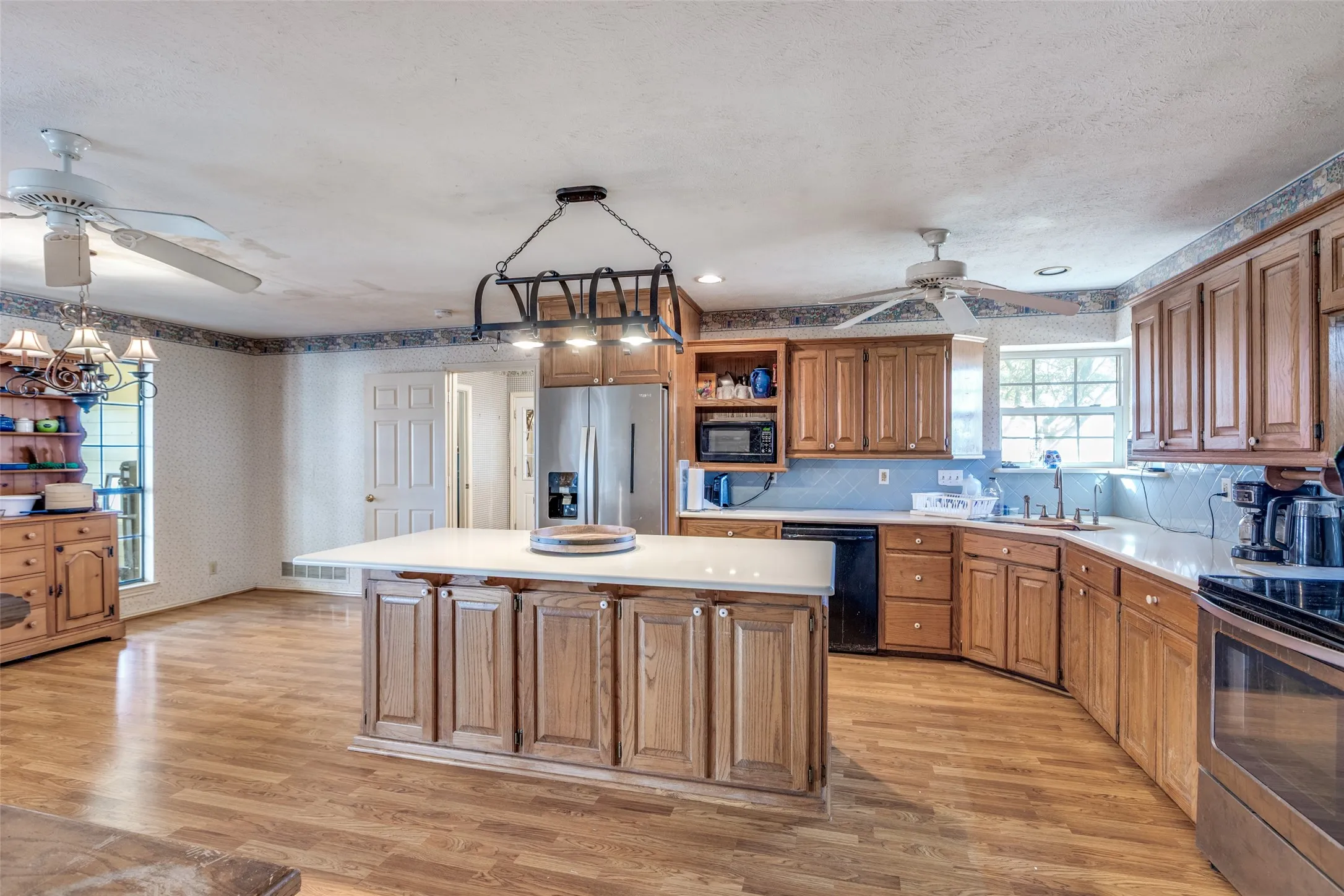 Kitchen with wallpapered walls, wood finish cabinets, stainless steel appliances, light countertops, and open shelves