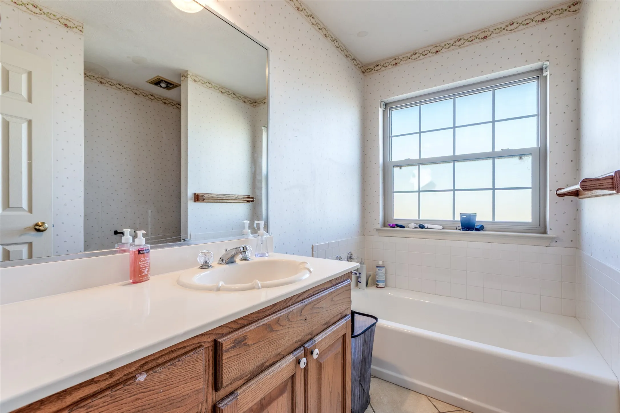 Bathroom featuring a garden tub, vanity, light tile patterned flooring, and wallpapered walls