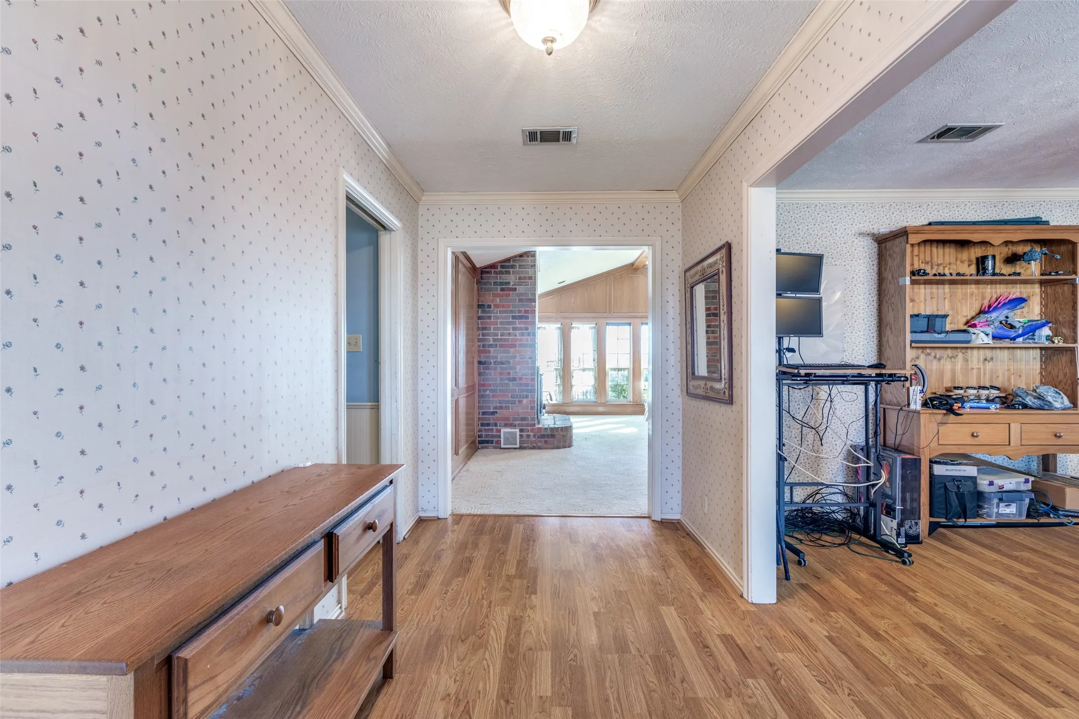 Corridor with light wood-type flooring, crown molding, and a textured ceiling