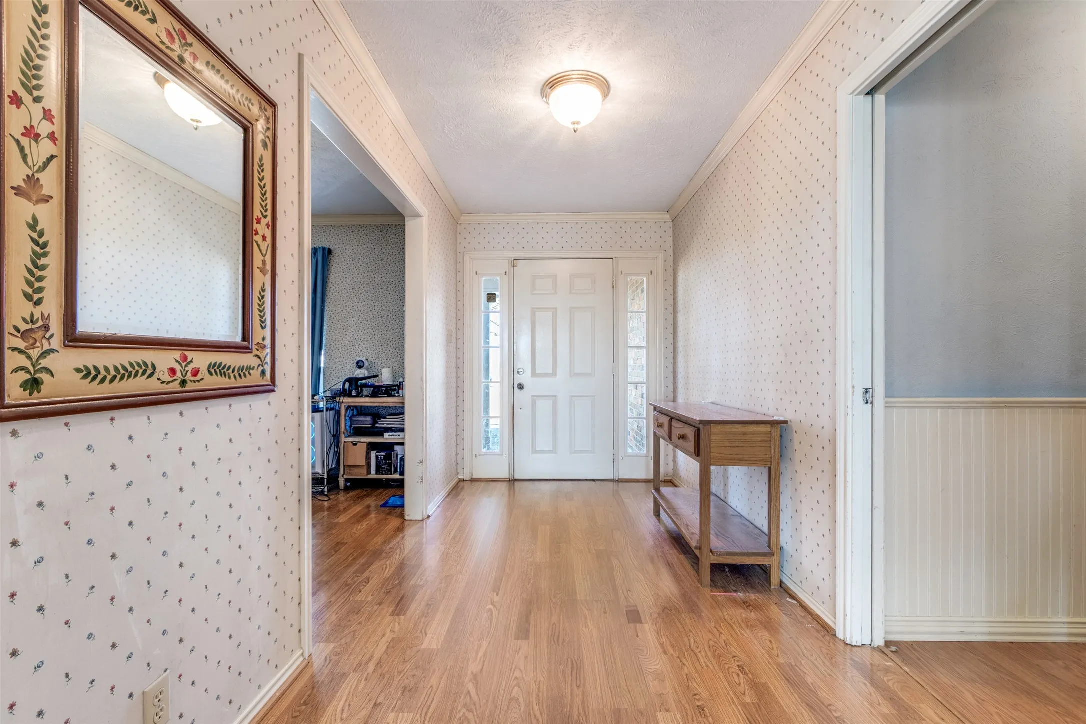 Foyer entrance with light wood-style flooring, crown molding, a textured ceiling, and wallpapered walls