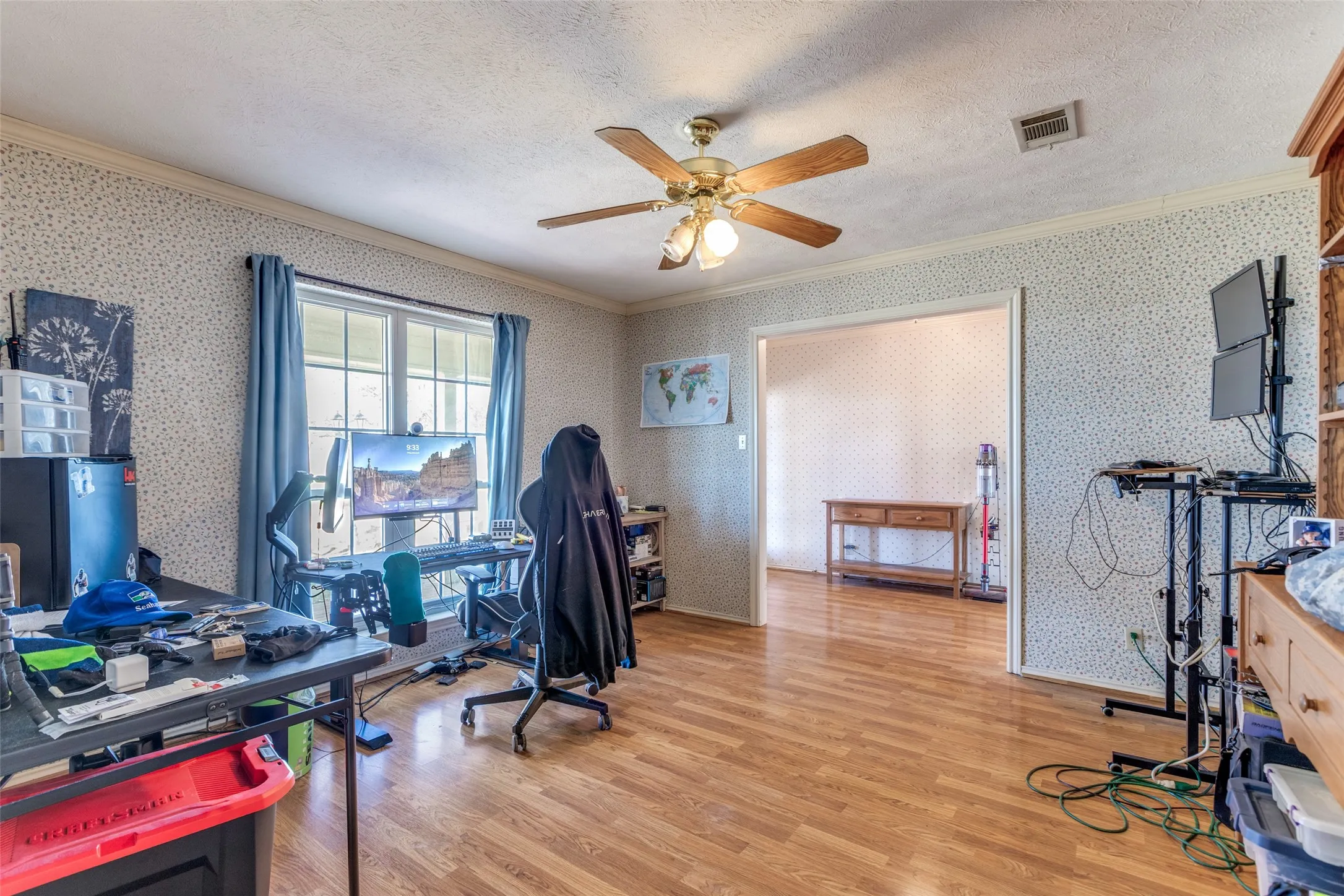 Office space featuring ceiling fan, light wood finished floors, crown molding, a textured ceiling, and wallpapered walls