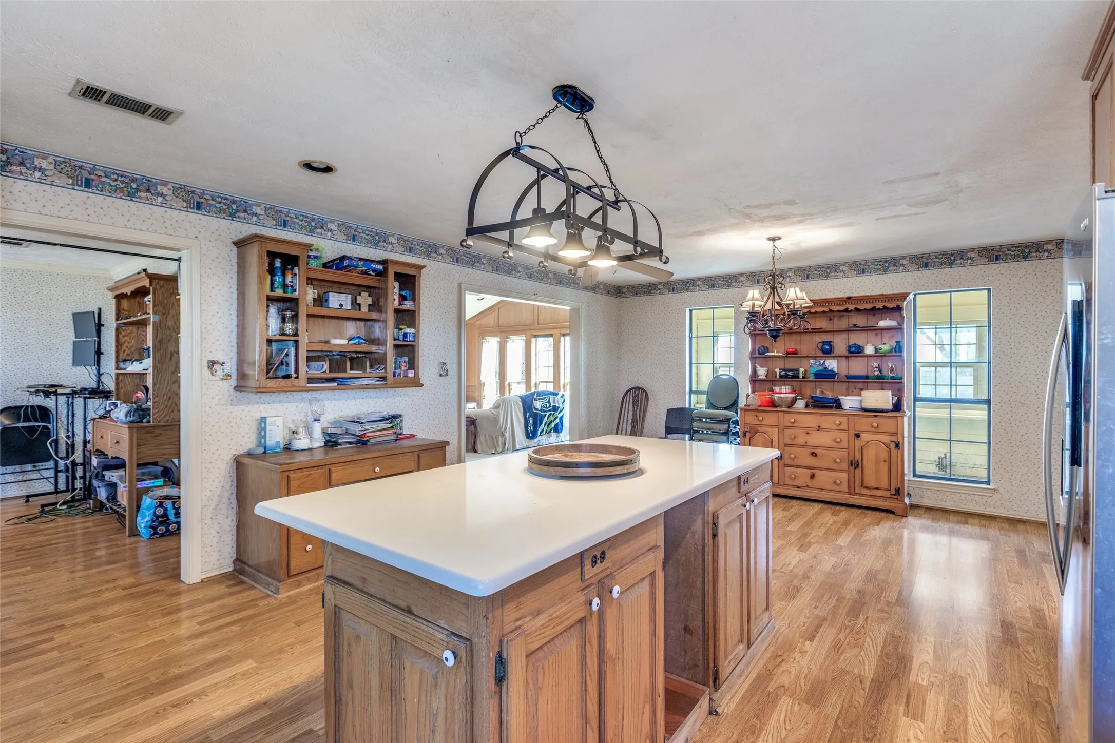 Kitchen featuring wallpapered walls, wood finish cabinets, a center island, light wood finished floors, and open shelves