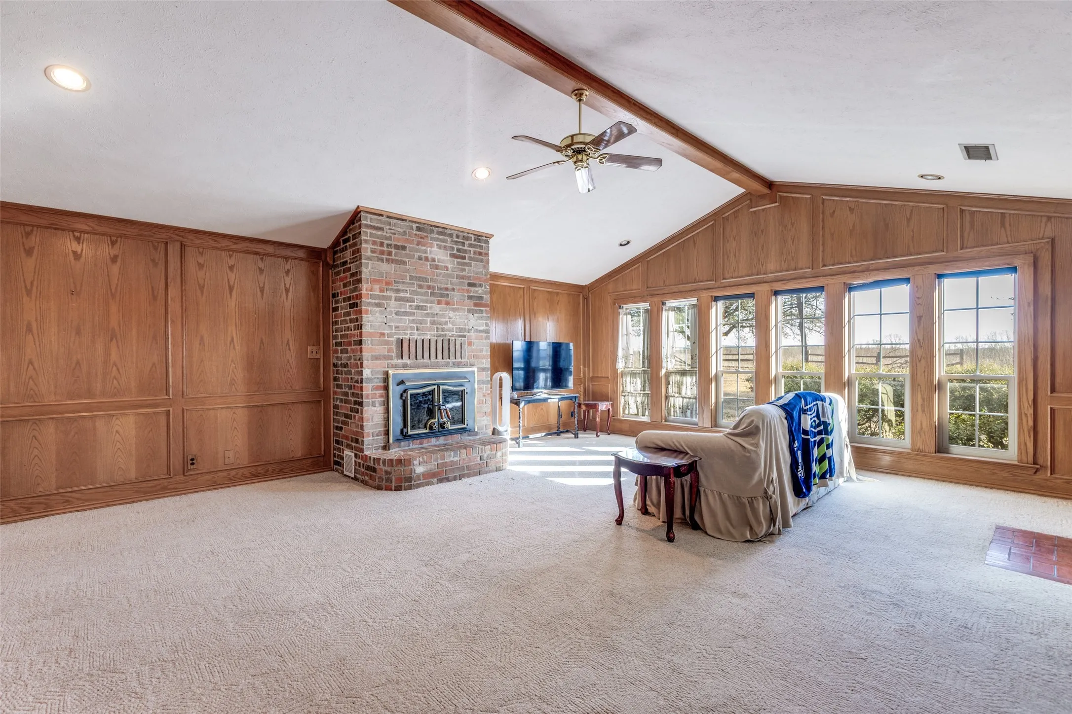 Living room featuring ceiling fan, carpet floors, wooden walls, beam ceiling, and a fireplace