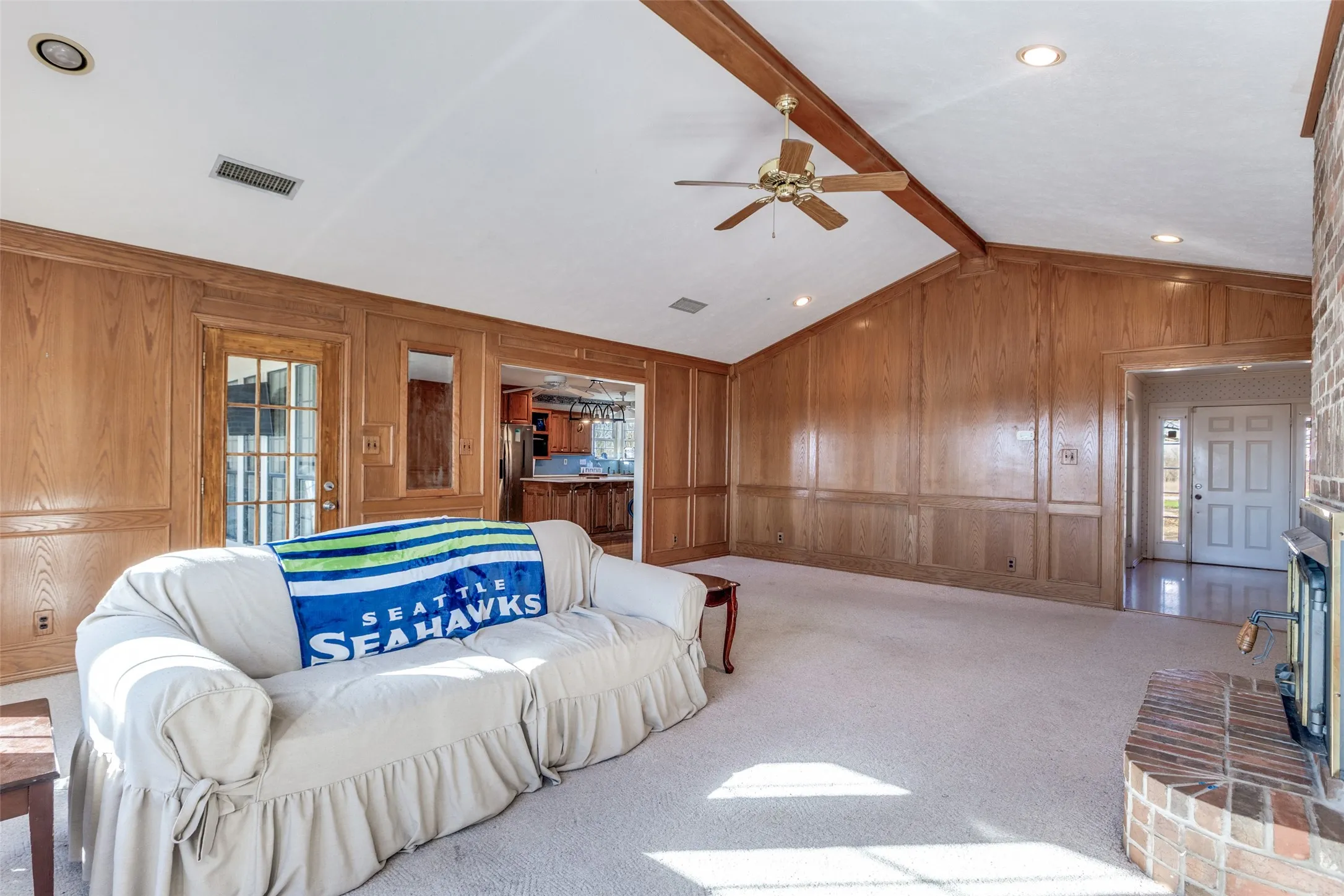 Living room featuring ceiling fan, carpet floors, wooden walls, beam ceiling, and a fireplace