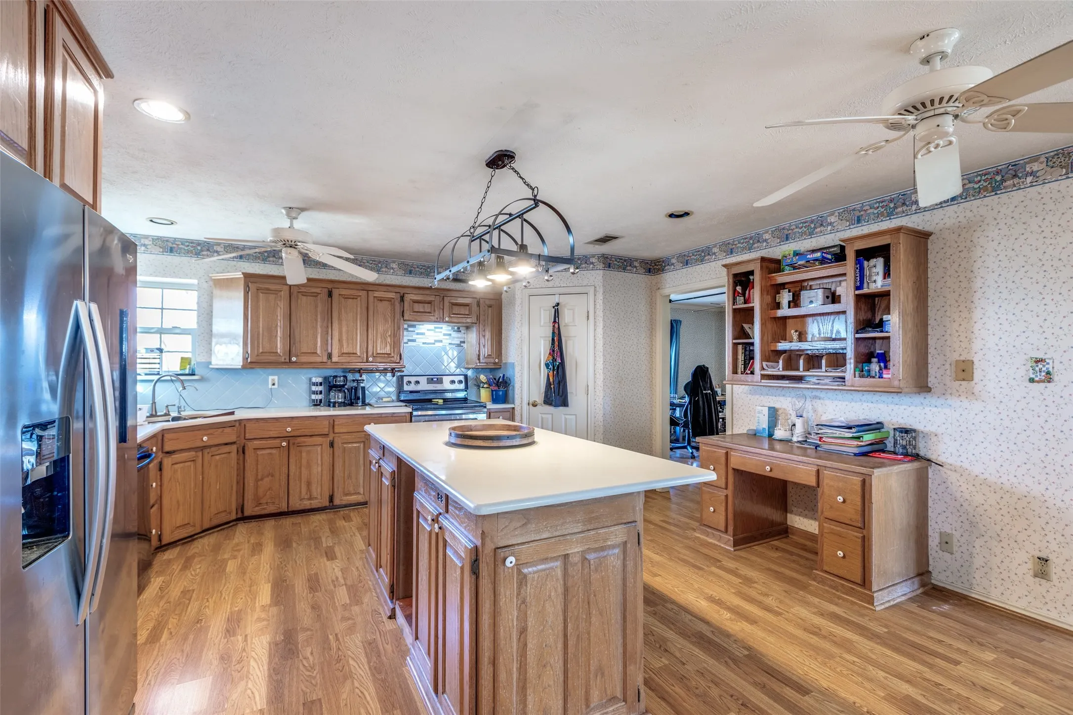 Kitchen with wallpapered walls, wood finish cabinets, stainless steel appliances, light countertops, and open shelves