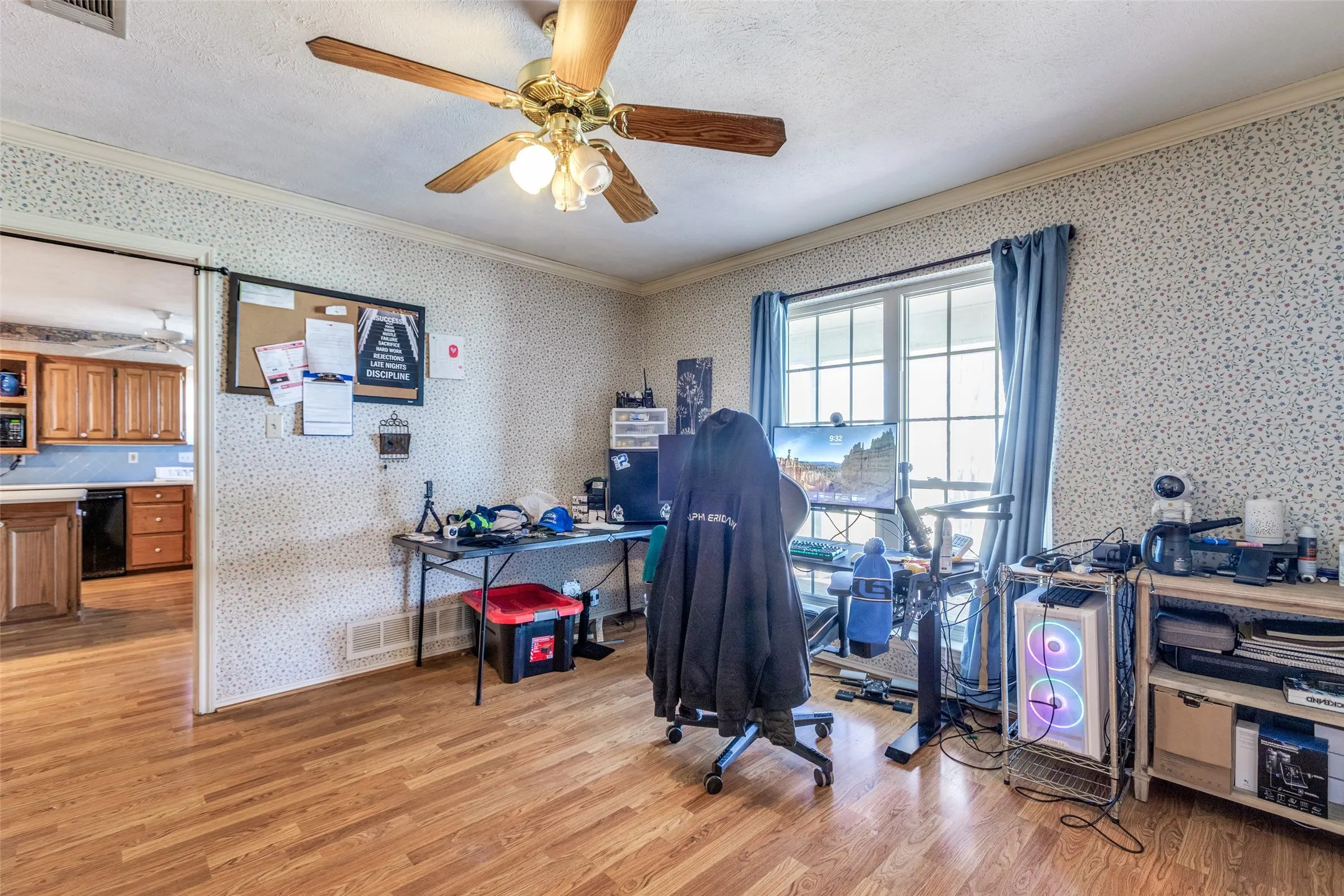 Office space featuring ceiling fan, light wood finished floors, crown molding, a textured ceiling, and wallpapered walls