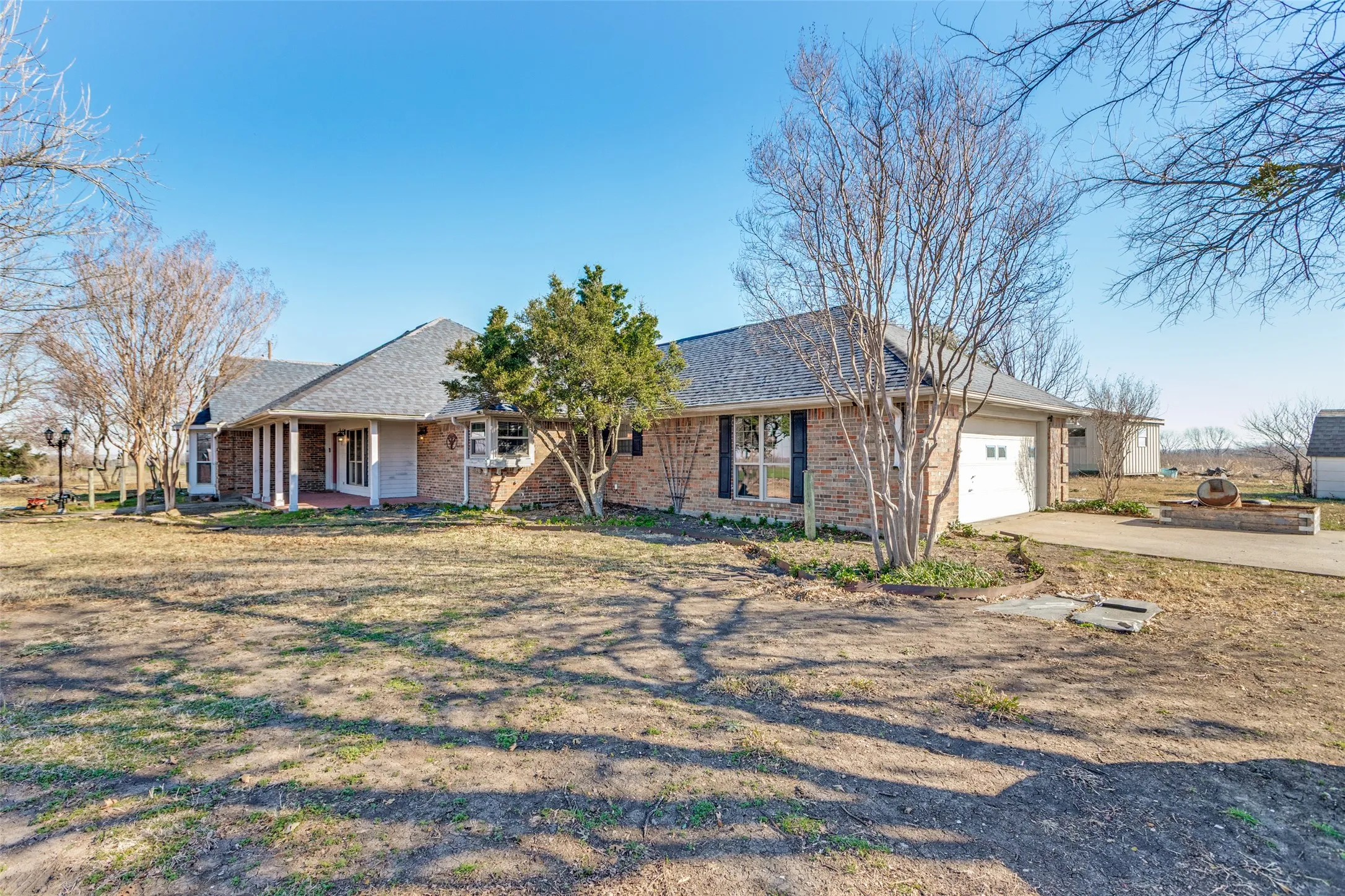 Ranch-style home with driveway, and attached garage, roof with shingles, and brick siding.