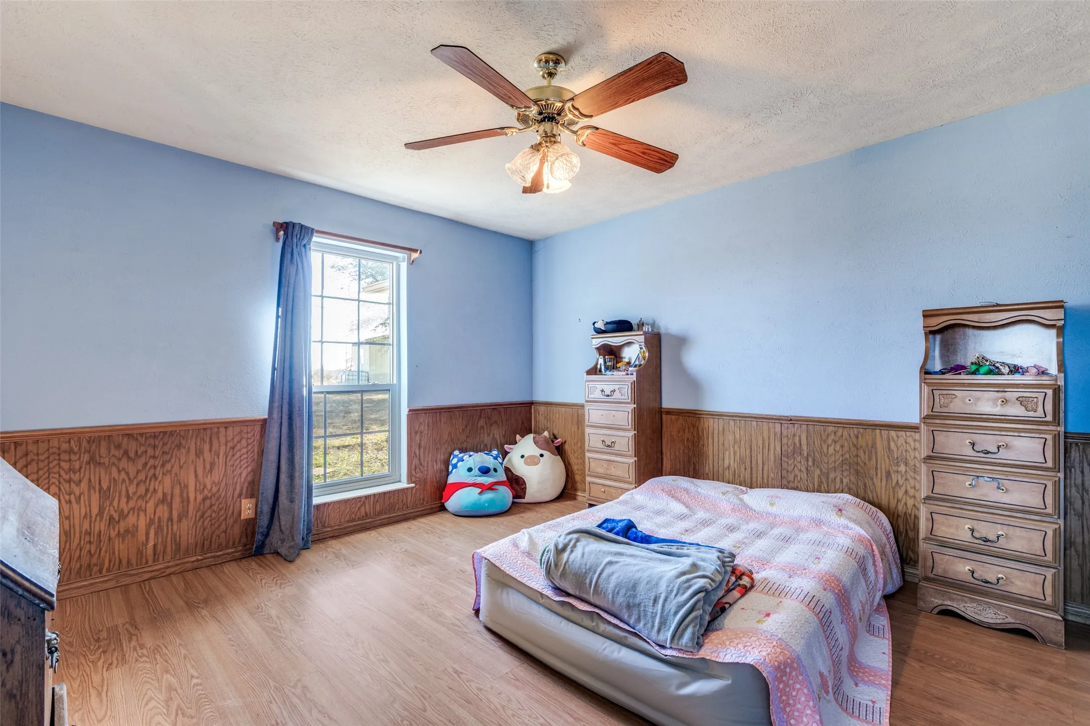 Bedroom featuring ceiling fan, a textured ceiling, wood finished floors, and a wooden wainscoted wall.