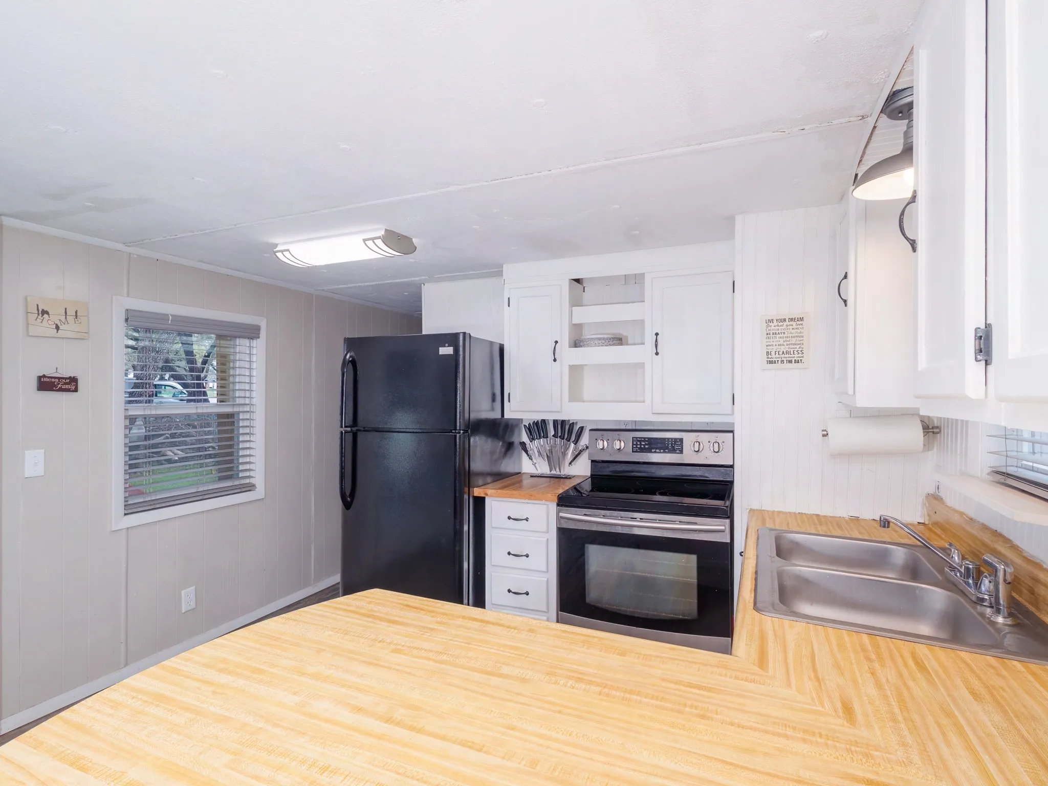 Kitchen featuring electric range, white cabinetry, freestanding refrigerator, open shelves, and wooden walls