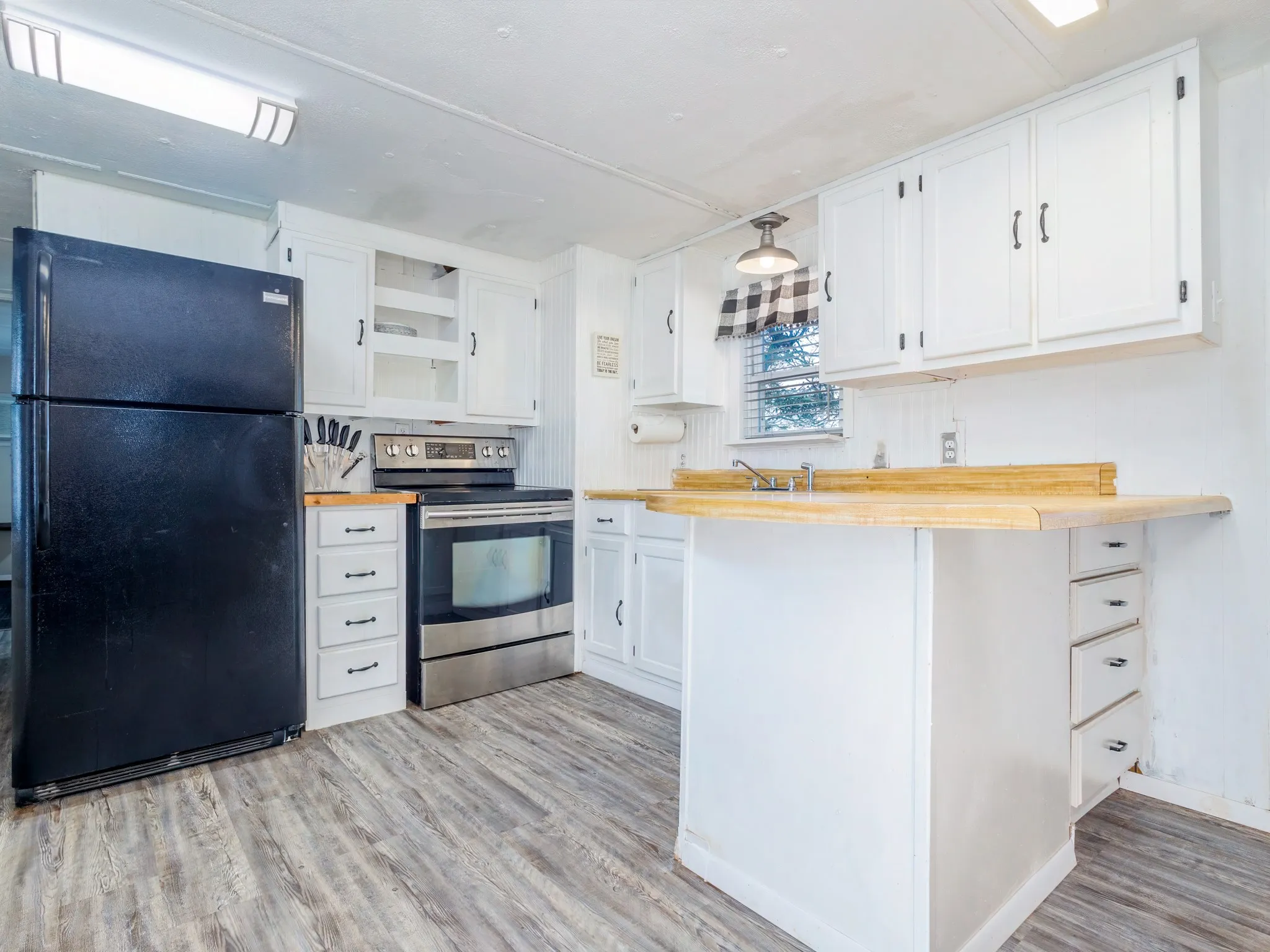 Kitchen with freestanding refrigerator, stainless steel electric range, white cabinetry, a peninsula, and light wood-type flooring