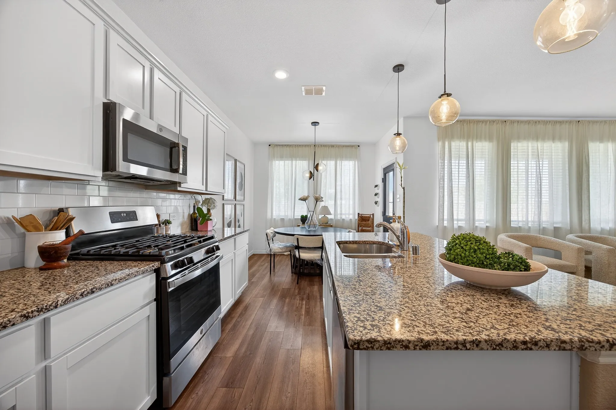 Kitchen featuring stainless steel appliances, dark stone countertops, a kitchen island with sink, and white cabinetry