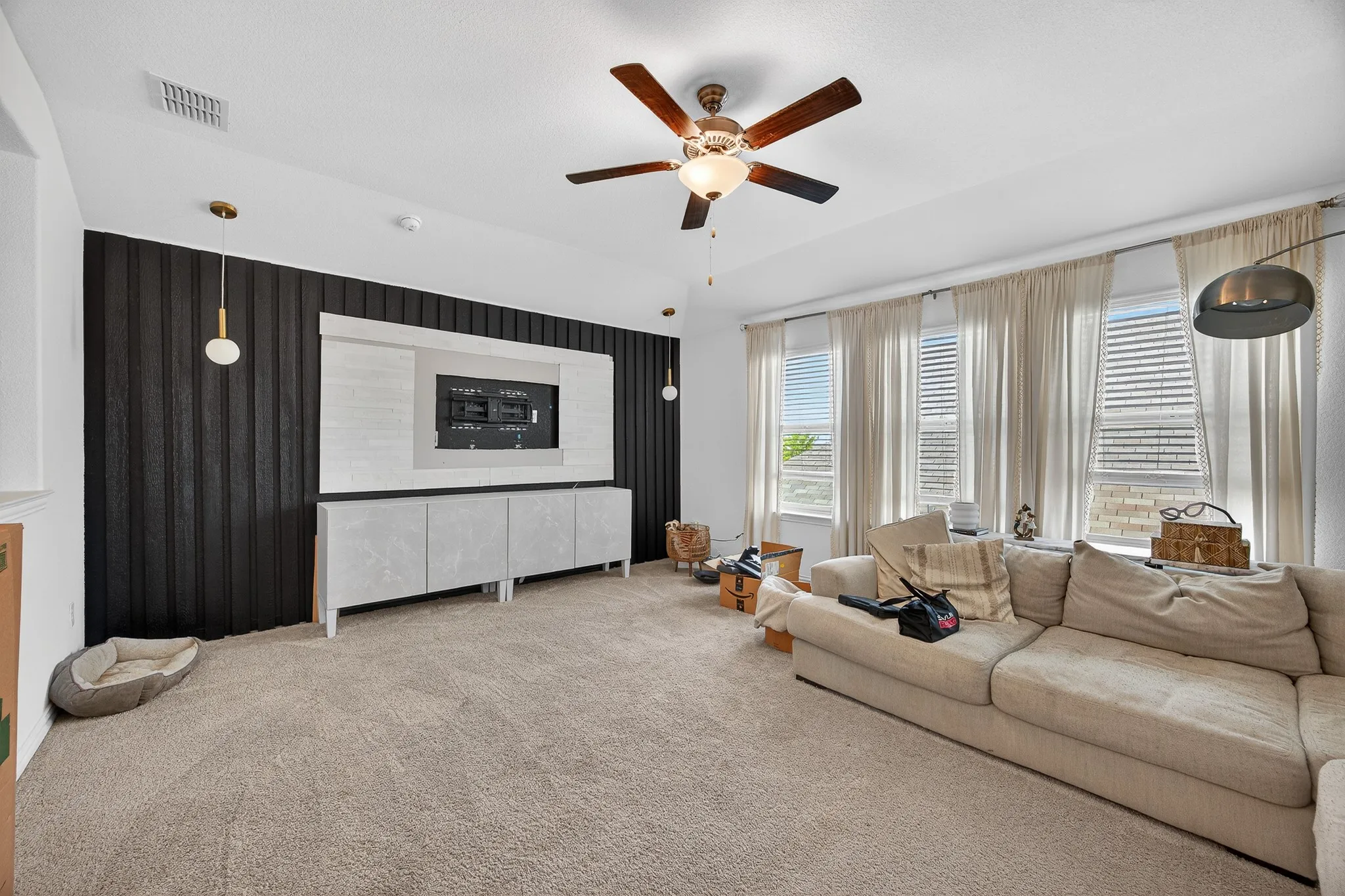 Living area with carpet floors, a ceiling fan, and an accent wall