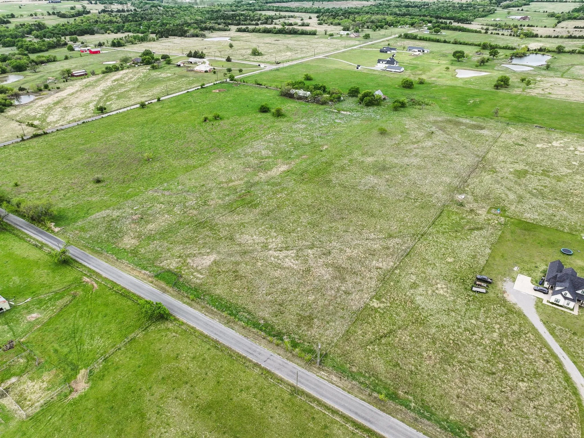 Expansive undeveloped land featuring varied green and brown vegetation, a paved road spanning the property, and visible fencing
