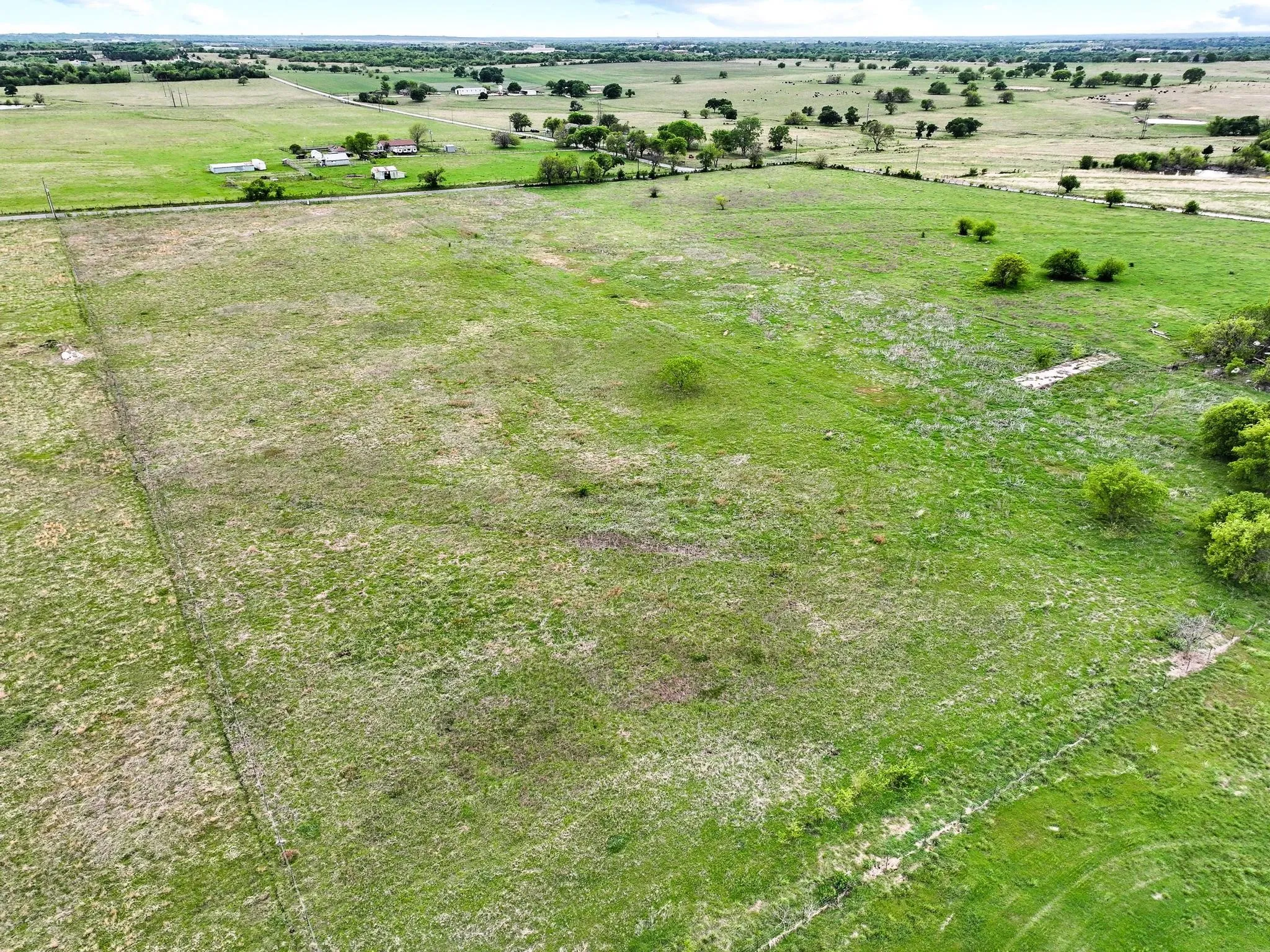 Expansive green acreage featuring scattered trees and a distant horizon of rural properties