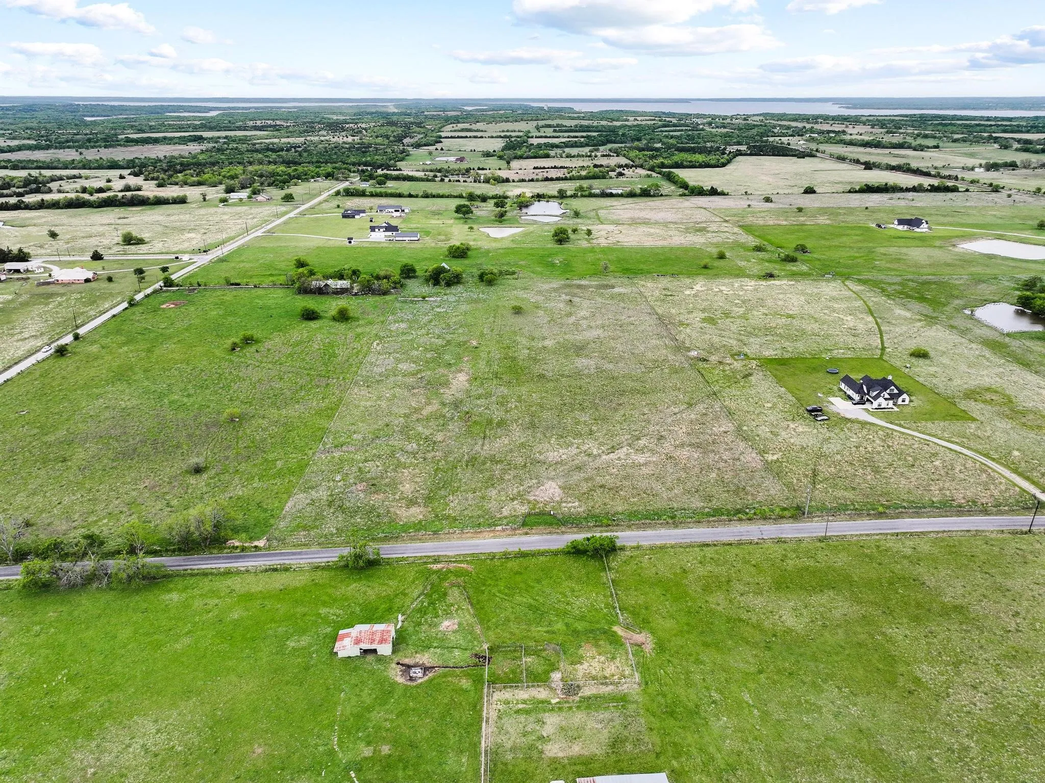 Expansive rural landscape featuring green fields, distant bodies of water, and scattered residential properties
